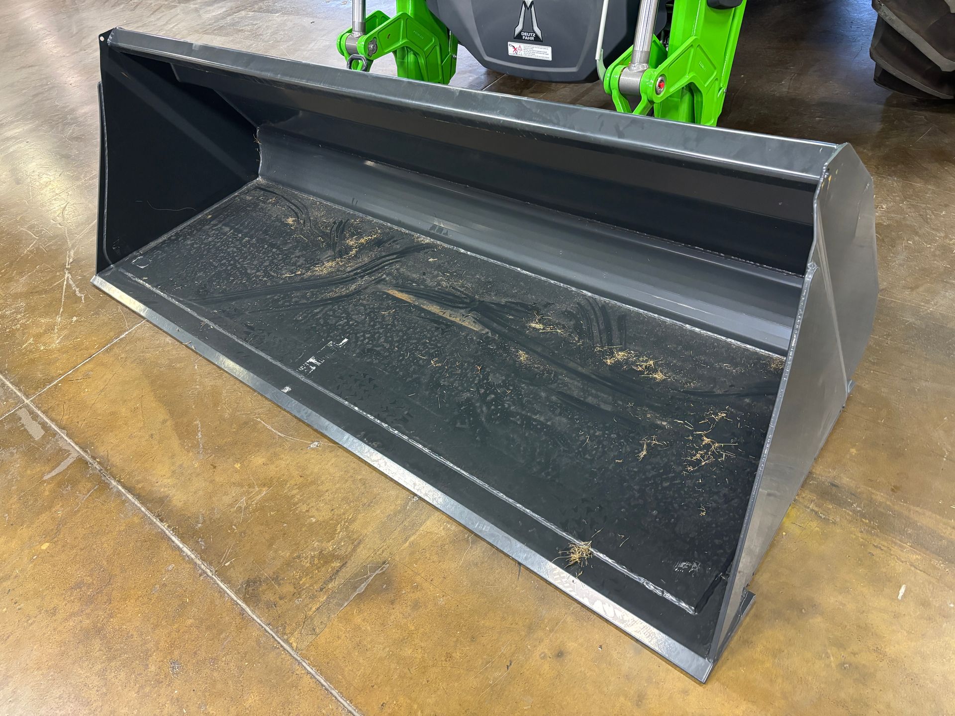 Black tractor bucket on a wood floor, with traces of dirt.