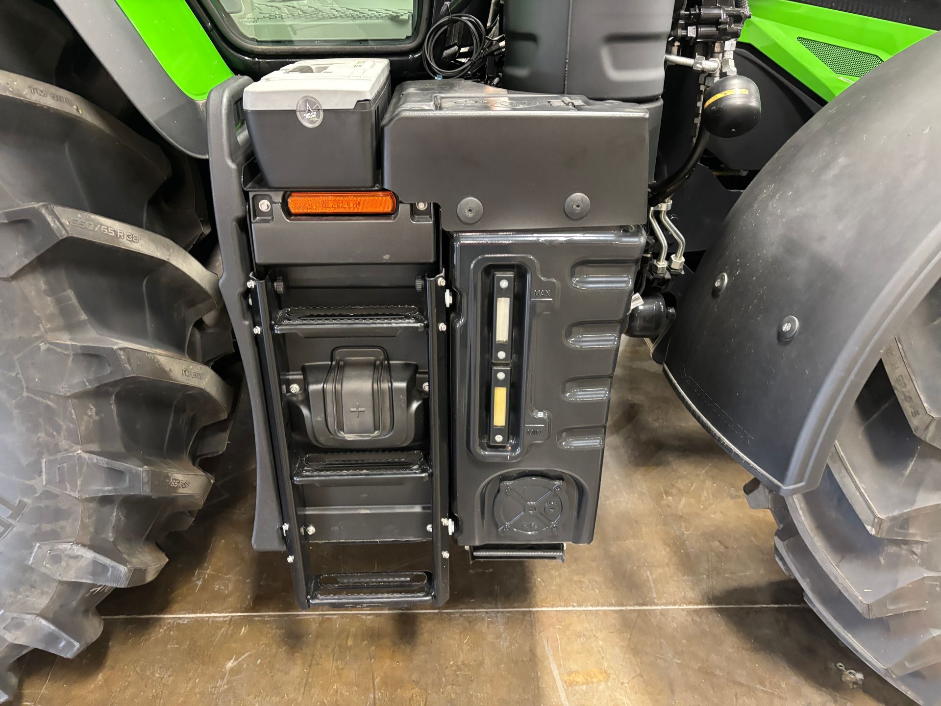 Black tractor side showing attached storage boxes and fuel/fluid gauge.