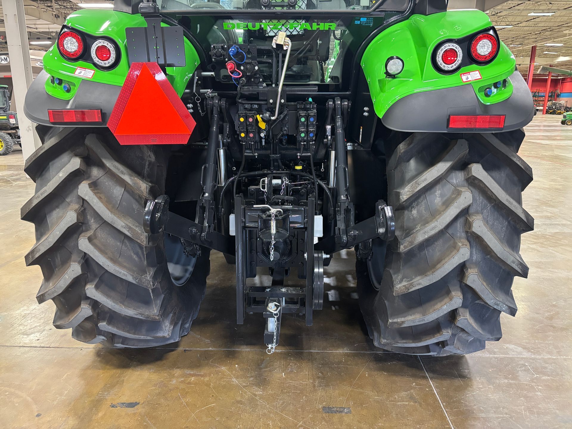 Rear view of a green and black tractor with large tires, a red triangle, and visible machinery.