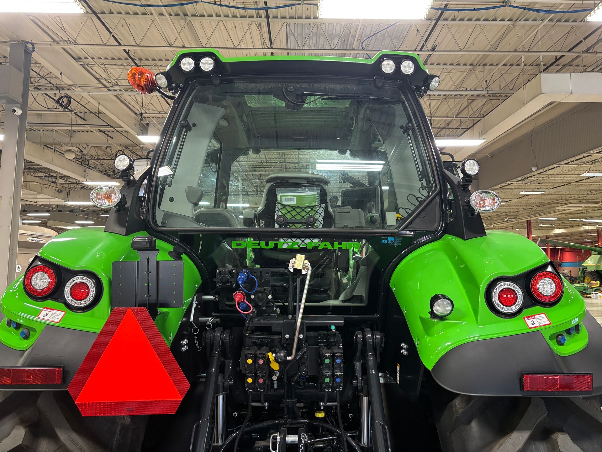 Back view of a green tractor with red safety triangle, taillights, and cabin lights.