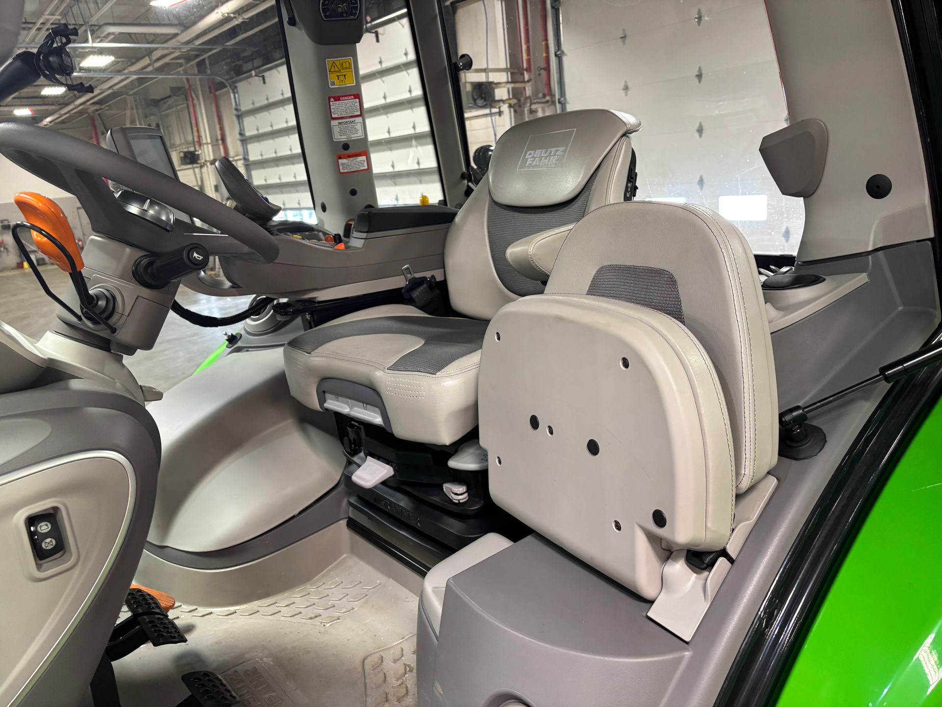 Interior of a tractor cab with gray and white seat, steering wheel, and controls.