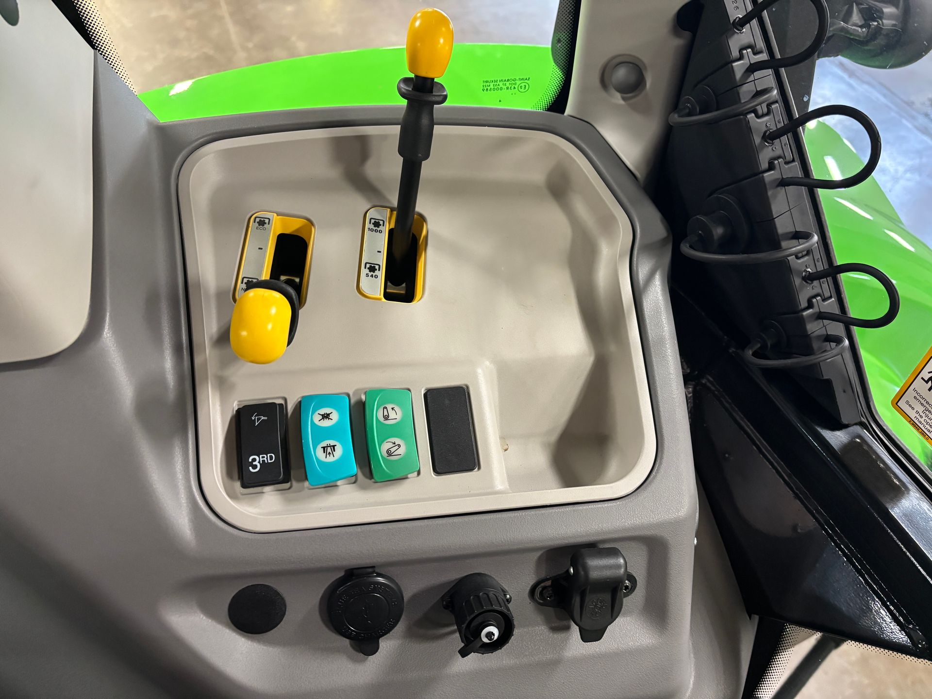 Interior view of a tractor console with levers, buttons, and switches, with a green exterior visible.
