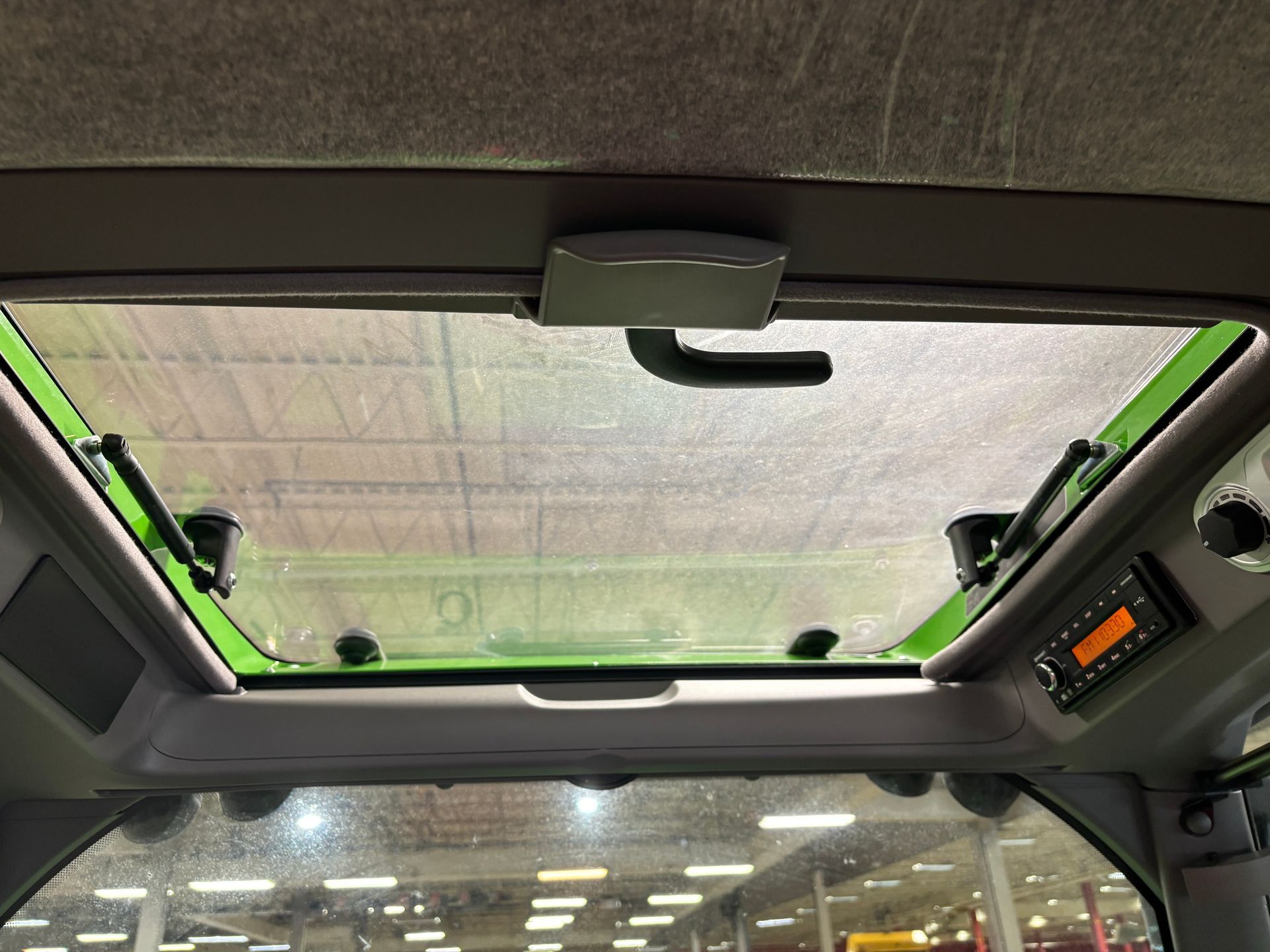 Interior view of a tractor cab with a clear sunroof, green trim, and a radio panel.