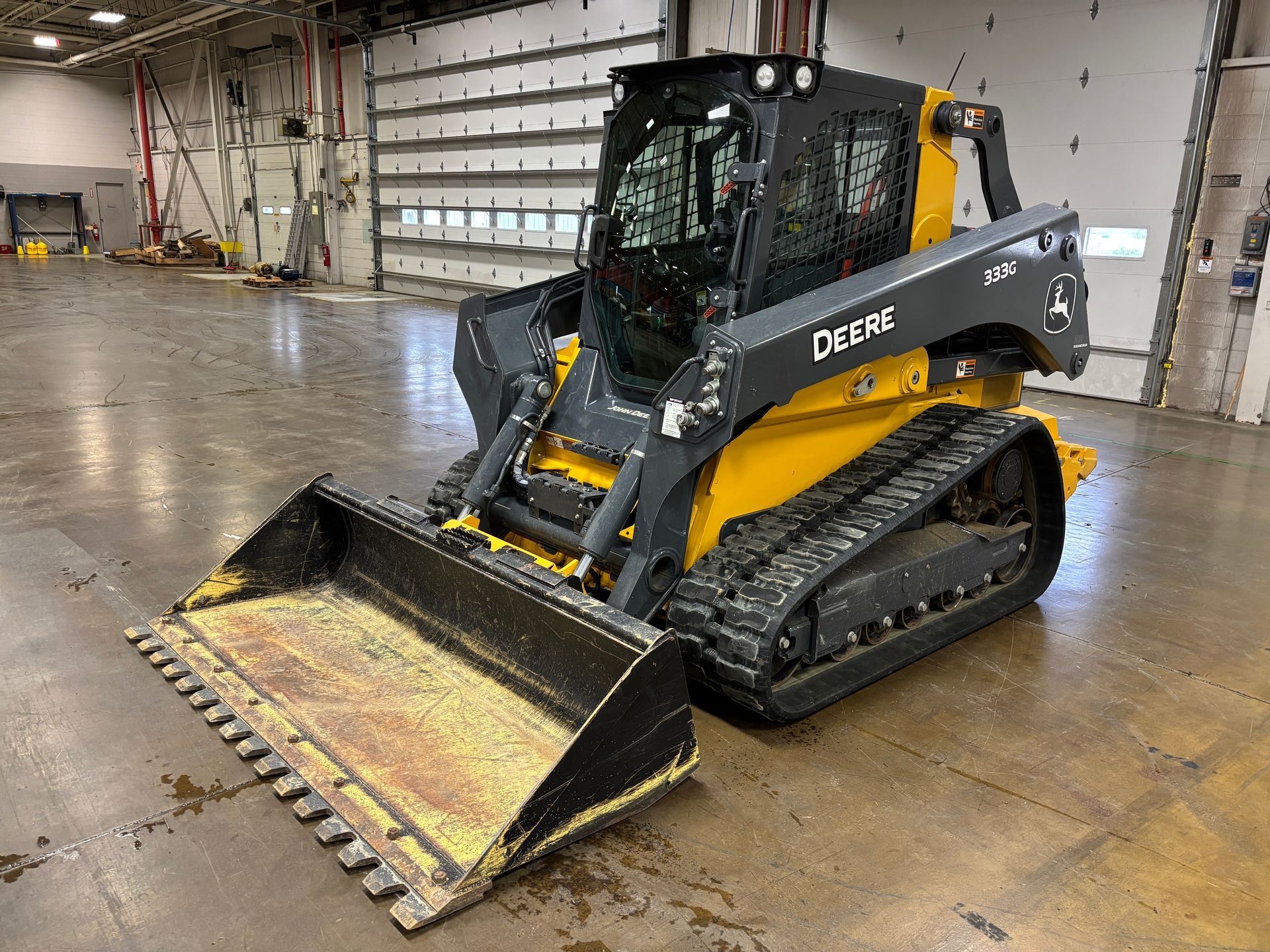 Yellow and black John Deere compact track loader with a bucket in an indoor setting.