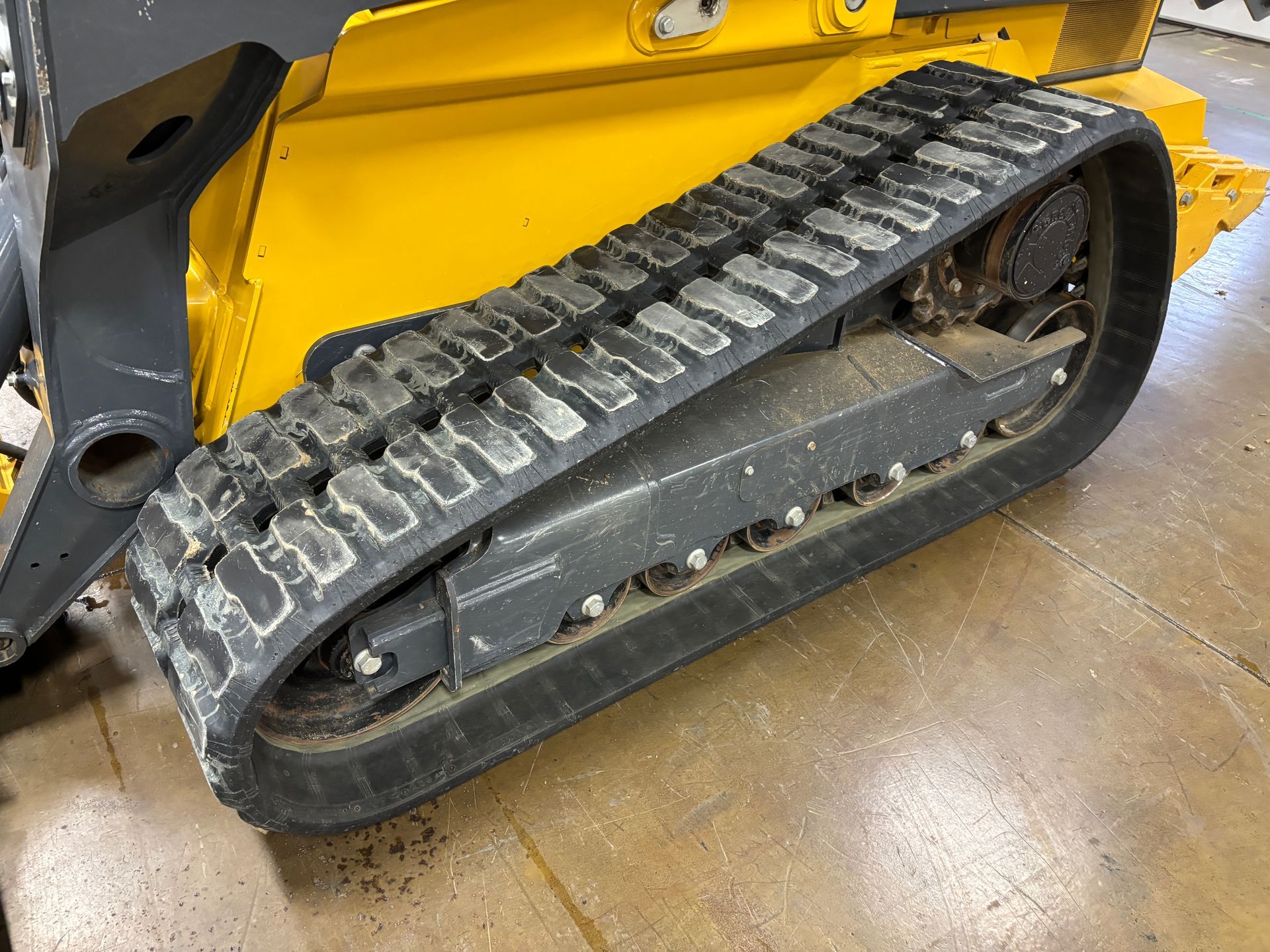 Yellow and black track of a skid steer loader on a concrete floor.