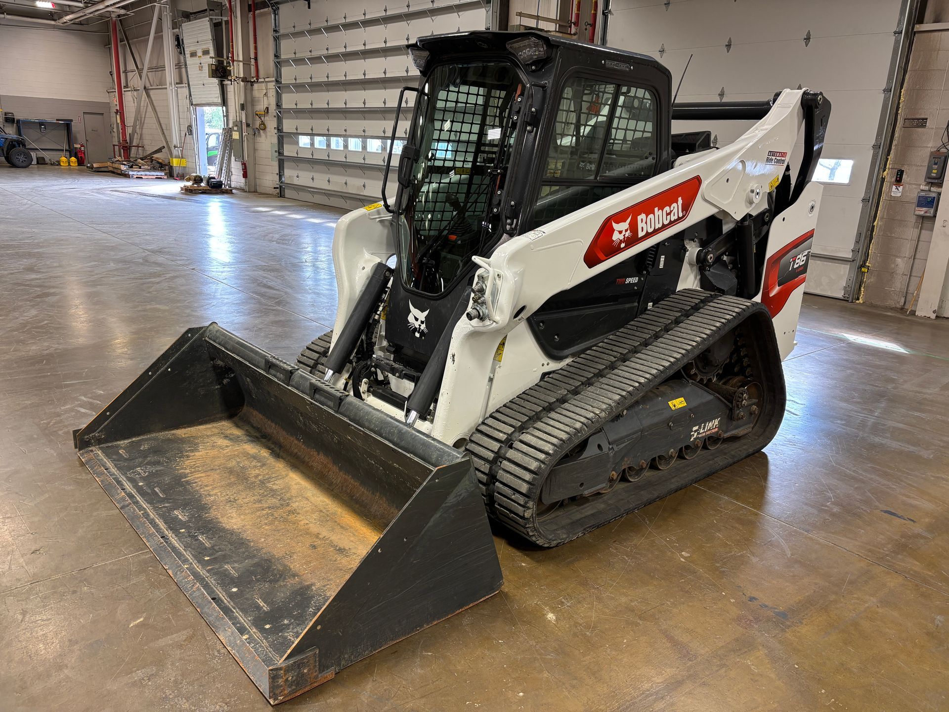 White Bobcat track loader with bucket in a warehouse.