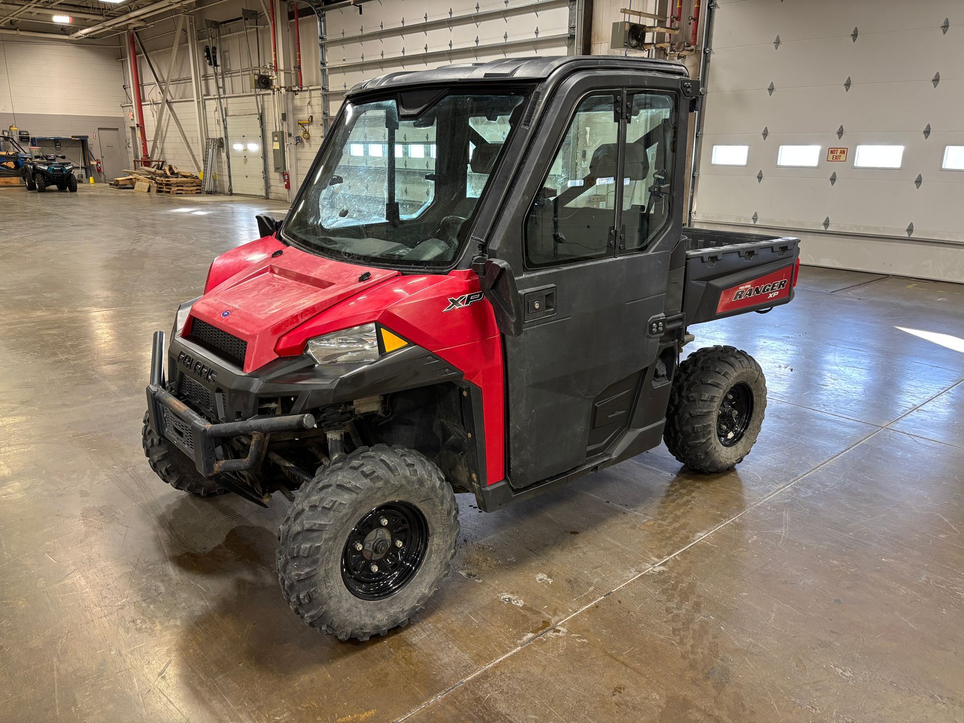 Red Polaris Ranger UTV with black roll cage and tires, parked indoors.