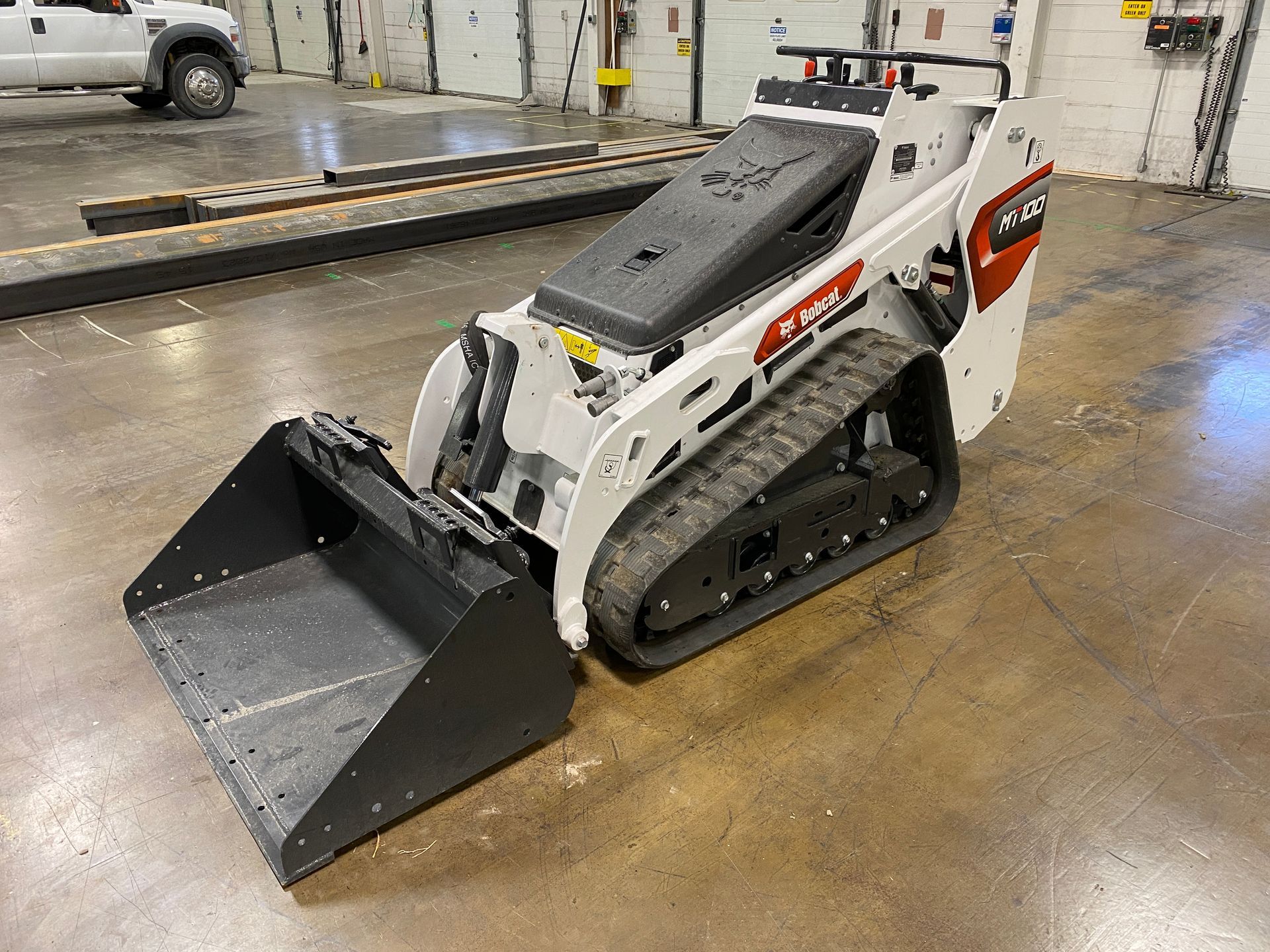 White Bobcat track skid steer with a black bucket in an indoor setting.