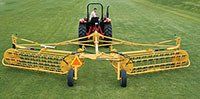 A yellow hay rake attached to a tractor on a grassy field.