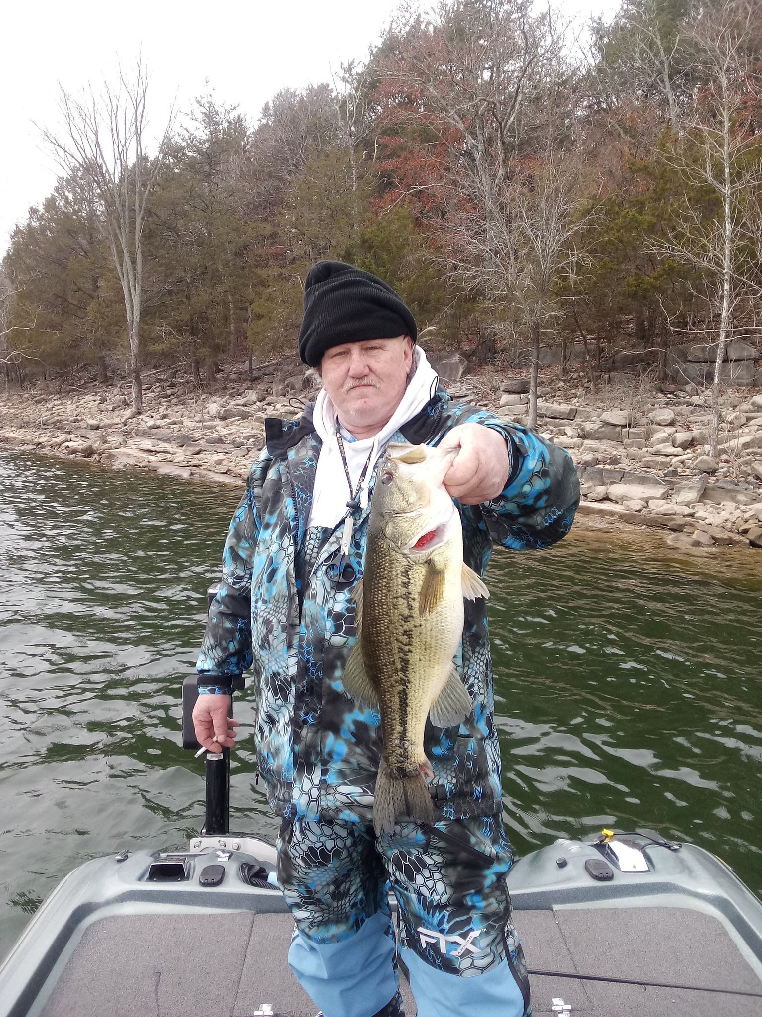A man is standing on a boat holding a large bass.