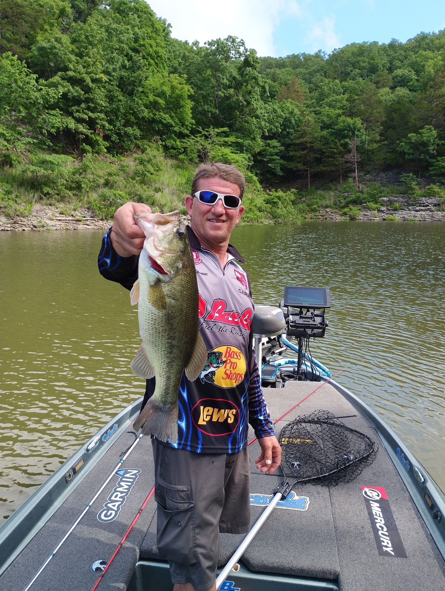 A man is standing on a boat holding a large bass.