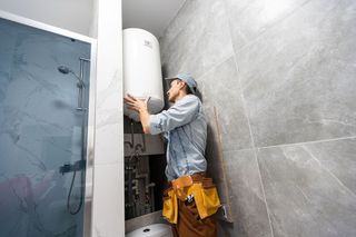 A man is installing a water heater in a bathroom.