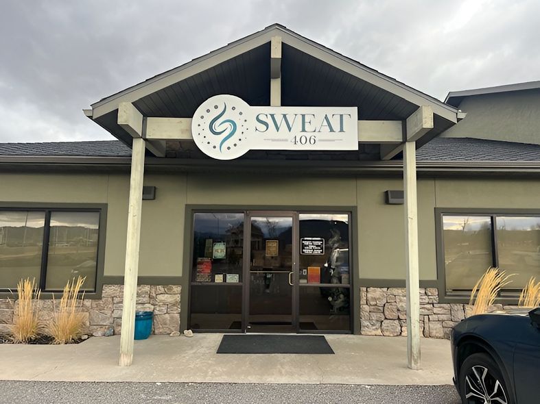 Exterior of the Sweat Lab building, featuring a green facade, stone base, and a prominent white circular sign.