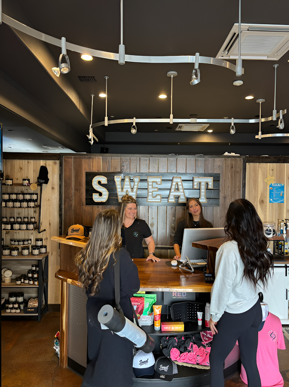 Two customers stand at a wooden counter talking to staff inside a gym with a prominent
