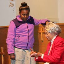 a woman in a red jacket is signing a book for a young girl in a purple jacket .