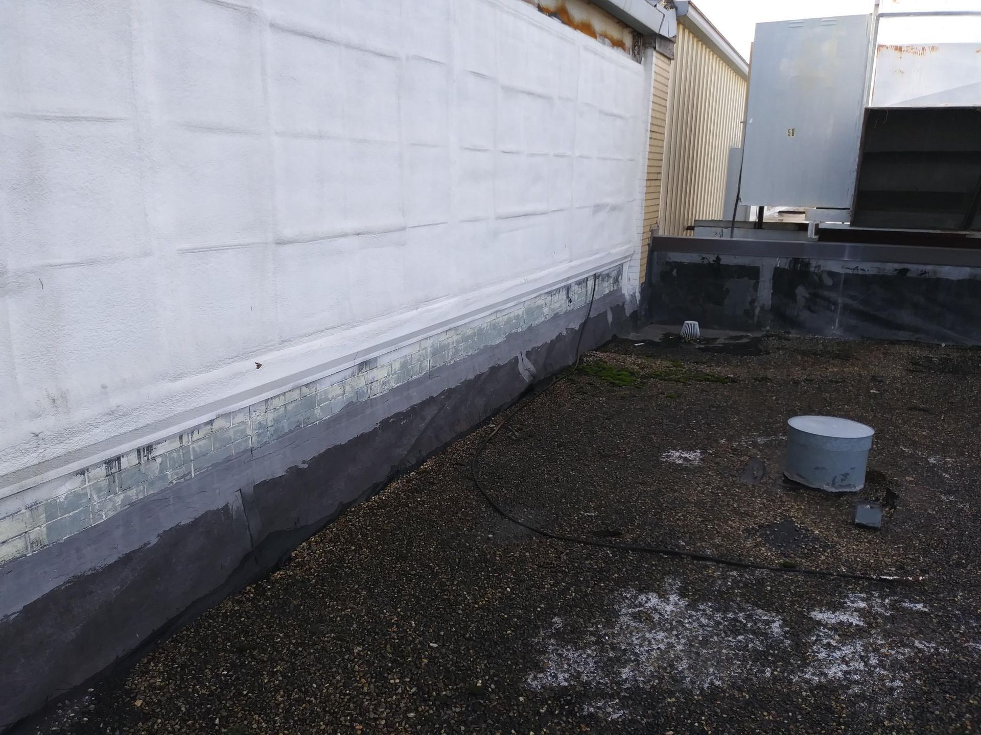 A roof with a drain on it and a white wall in the background.