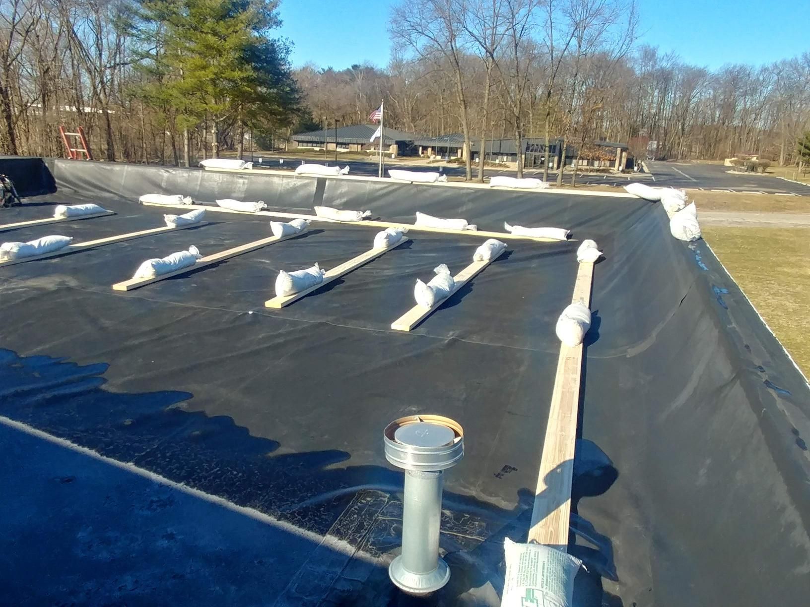 A black tarp is covering a roof with trees in the background