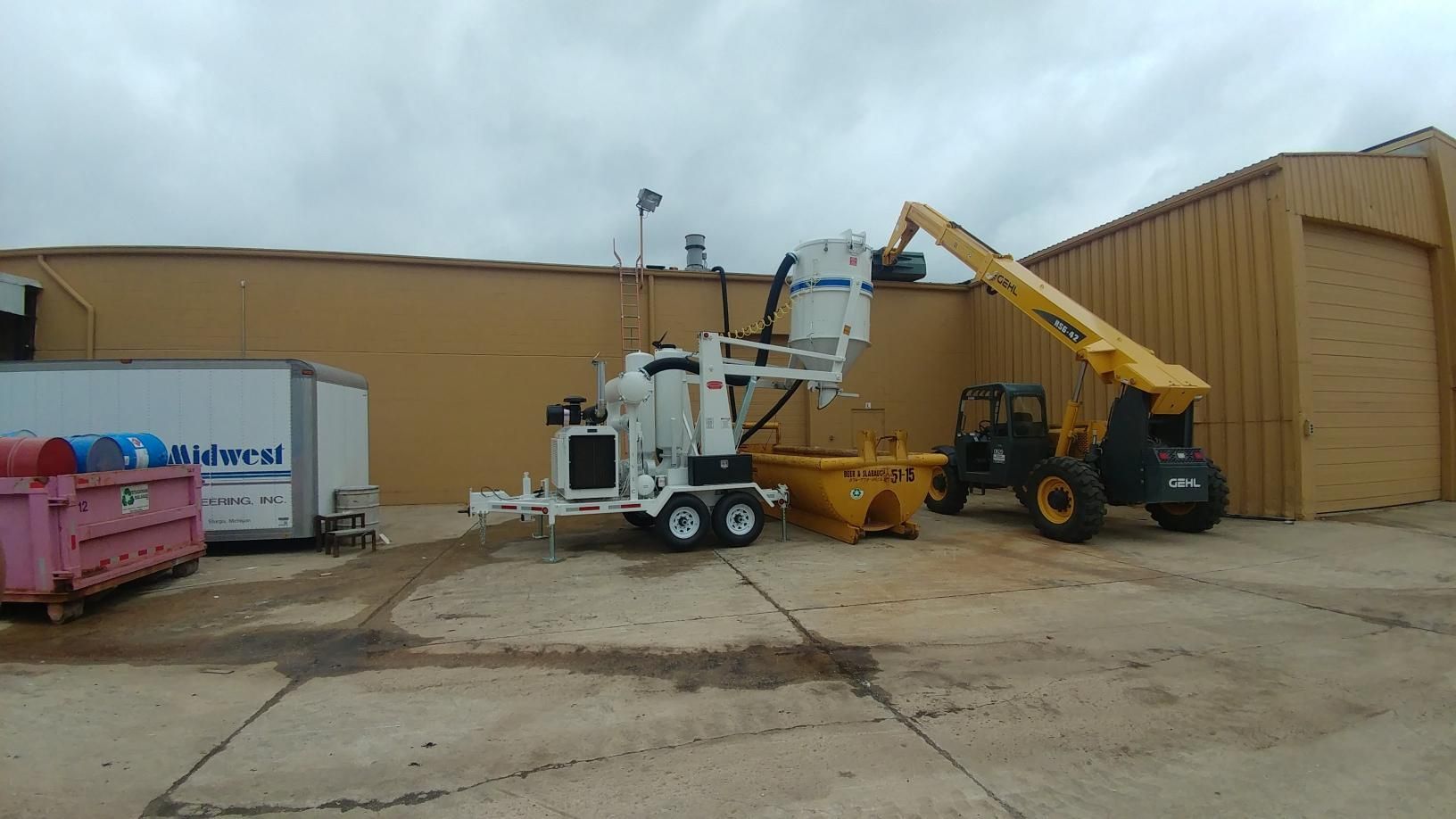 A trailer with a bucket on it is parked in front of a building.
