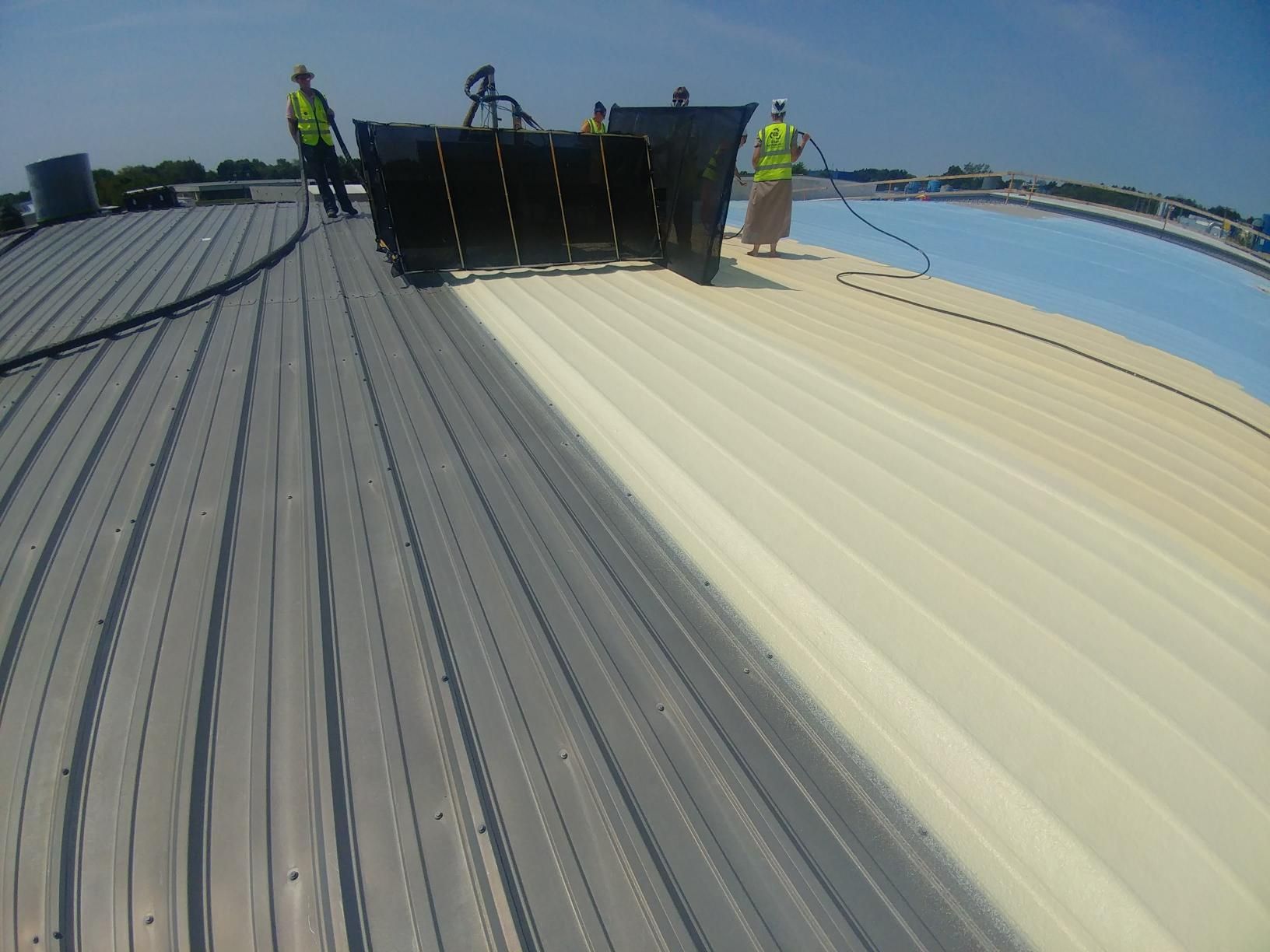 A group of people are spraying a roof with a hose.