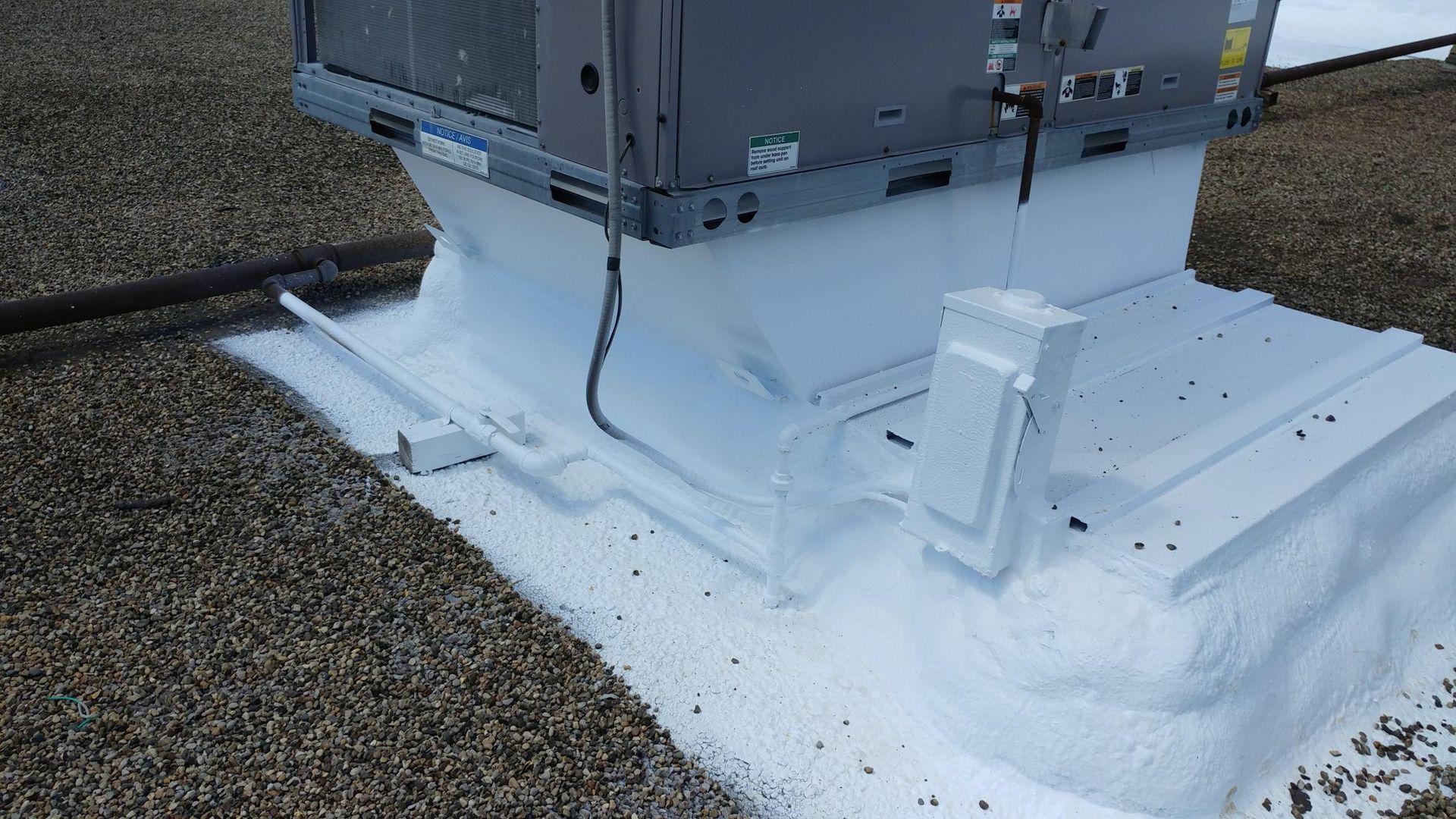 A large air conditioner is sitting on top of a gravel roof.