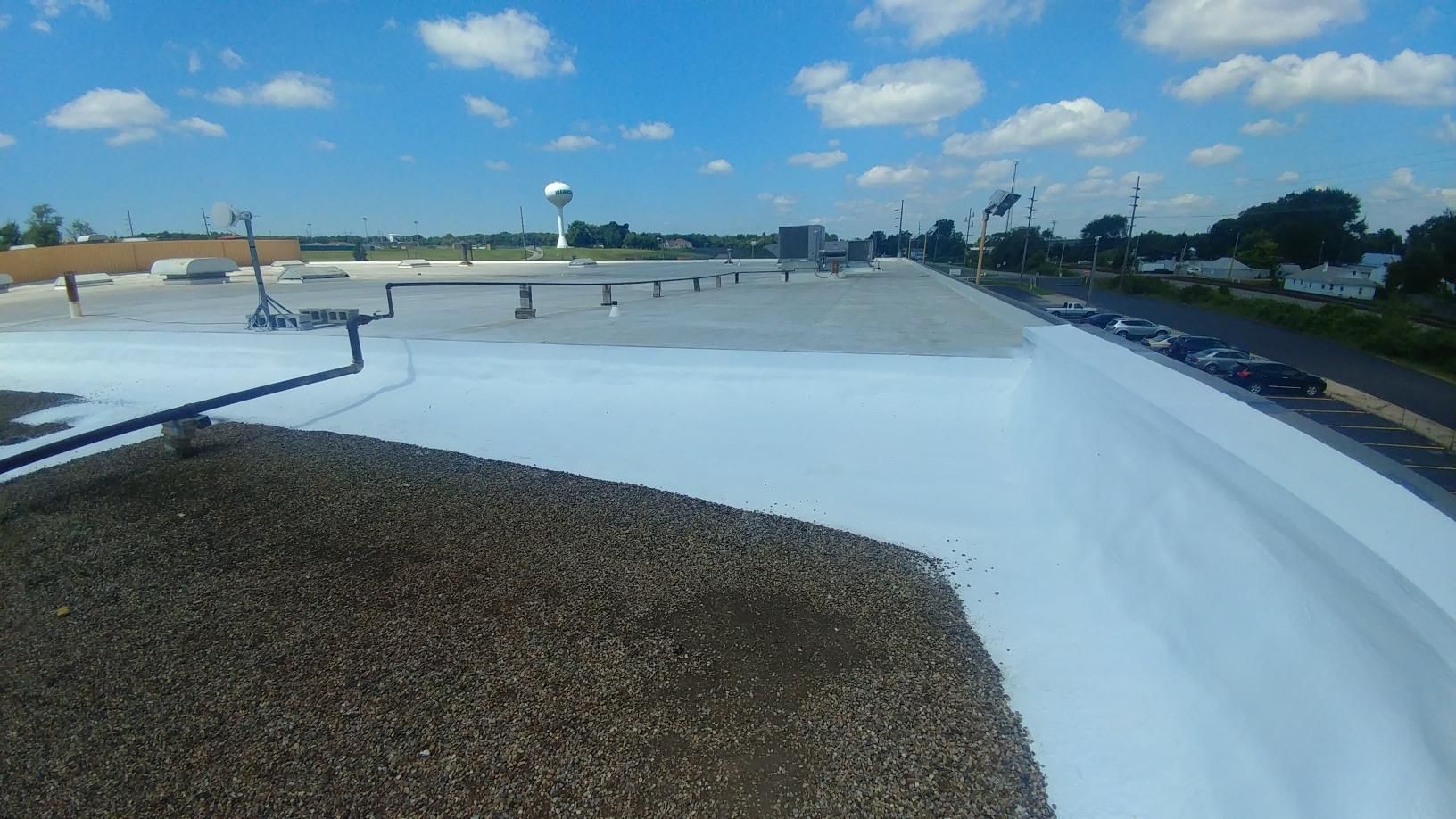 A roof with a white coating on it and a water tower in the background.