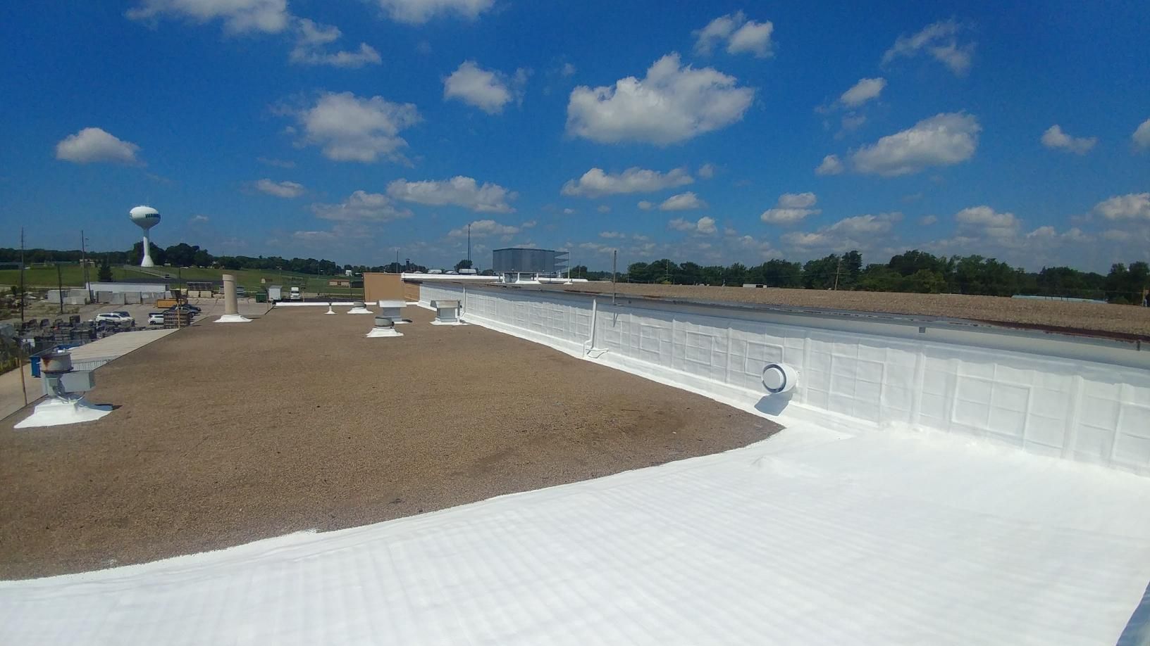 A white roof with a water tower in the background on a sunny day.