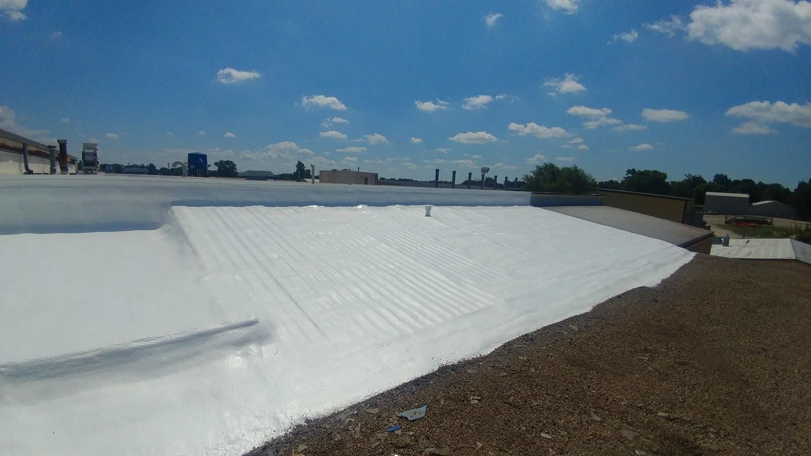 A large white roof is being painted on a sunny day.