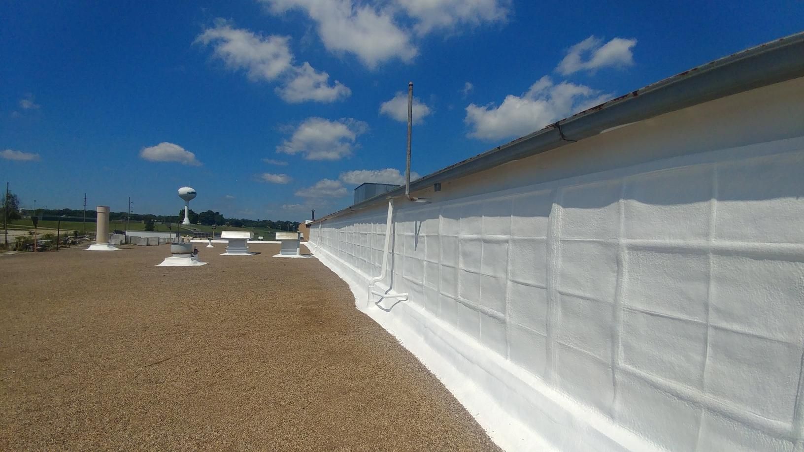 A roof with a lot of gravel on it and a water tower in the background.