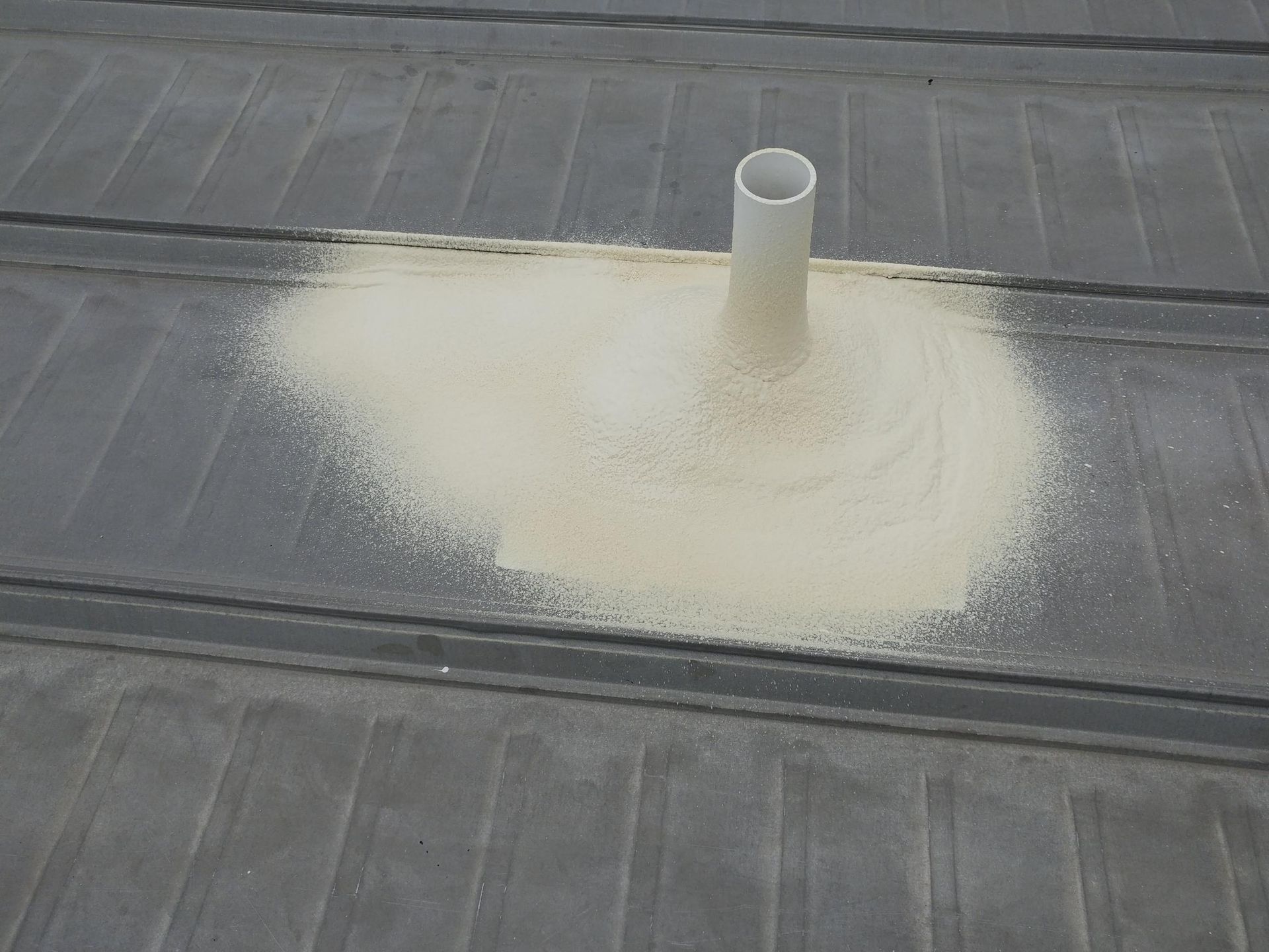 A white pipe is sitting on top of a pile of sand on a roof.