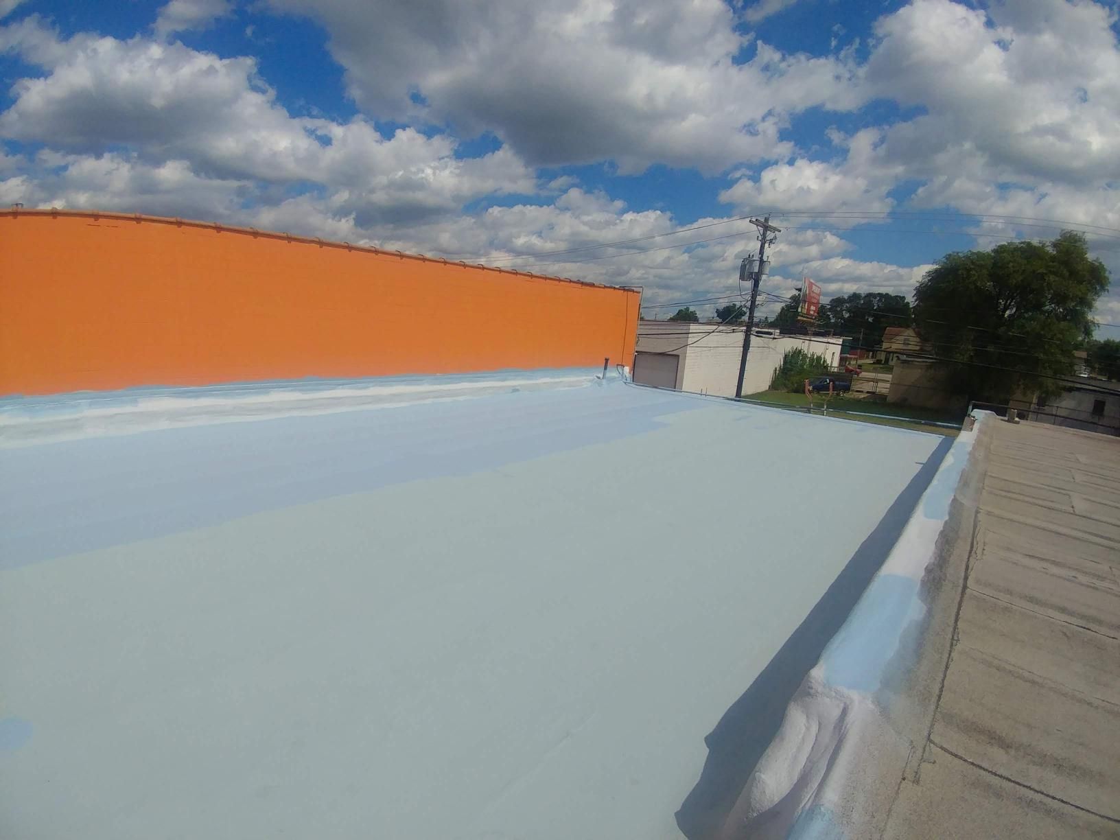 A roof with a blue coating on it and an orange building in the background.