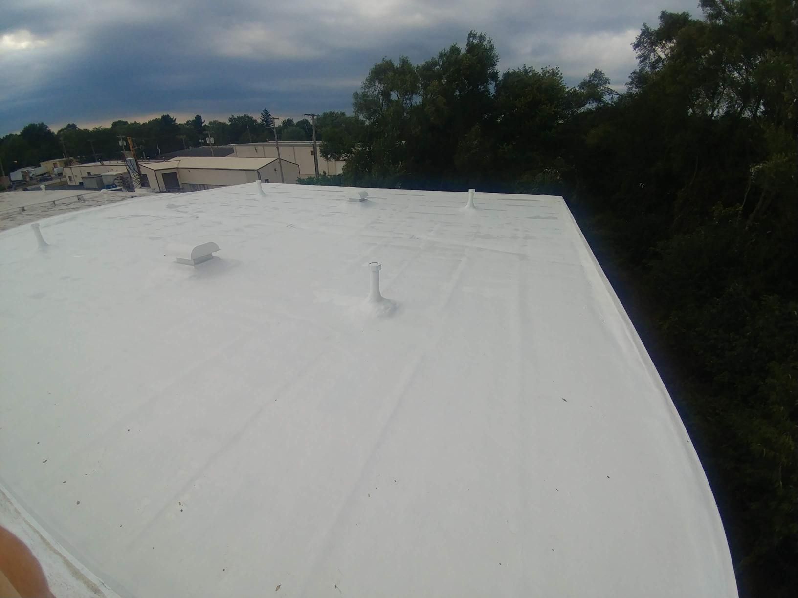 A person is standing on top of a white roof with trees in the background.