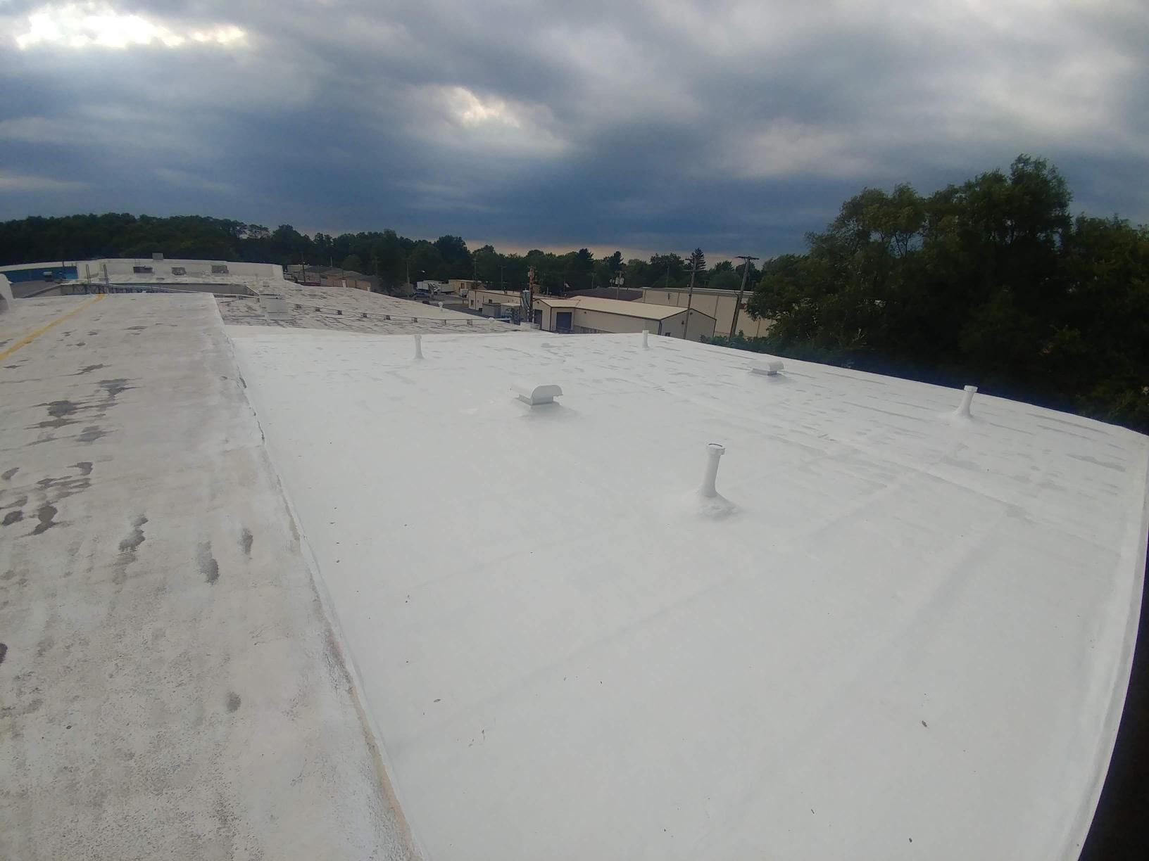 A white roof with trees in the background and a cloudy sky.