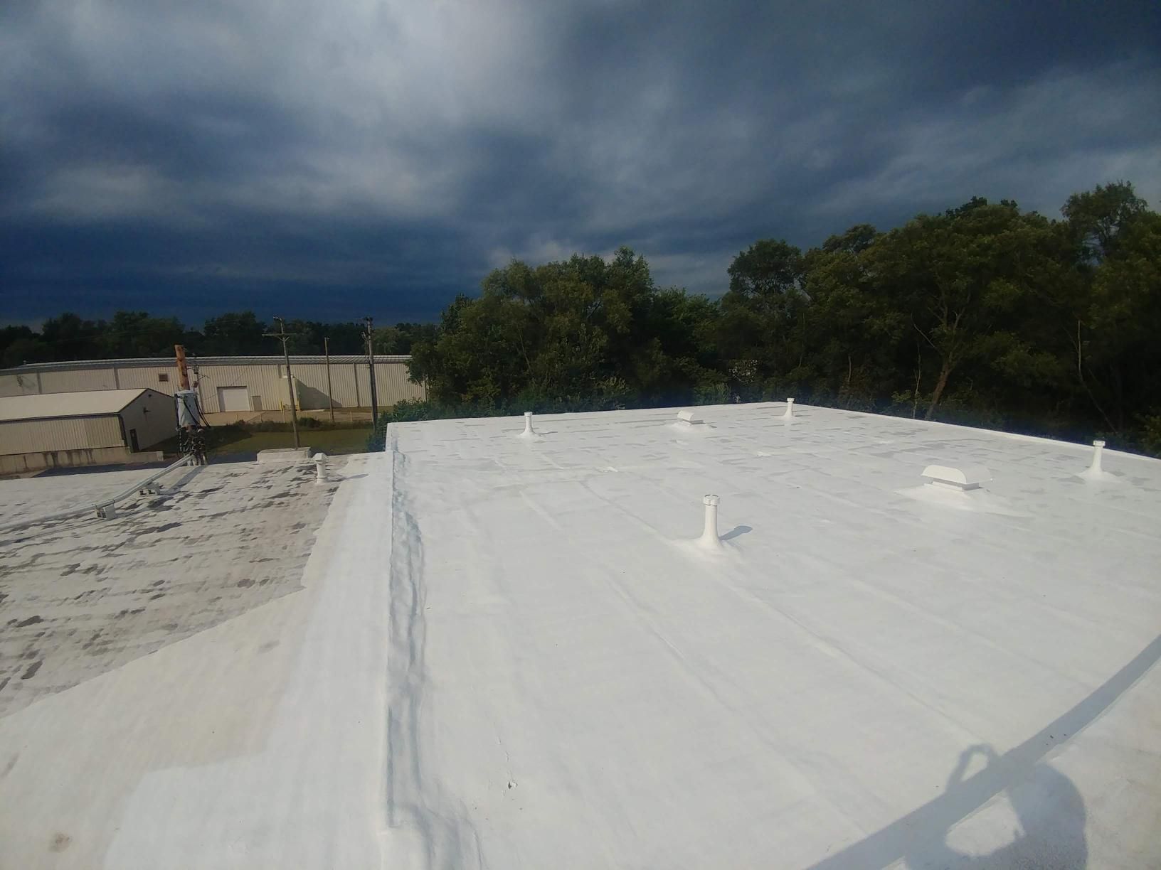 A white roof with trees in the background and a cloudy sky