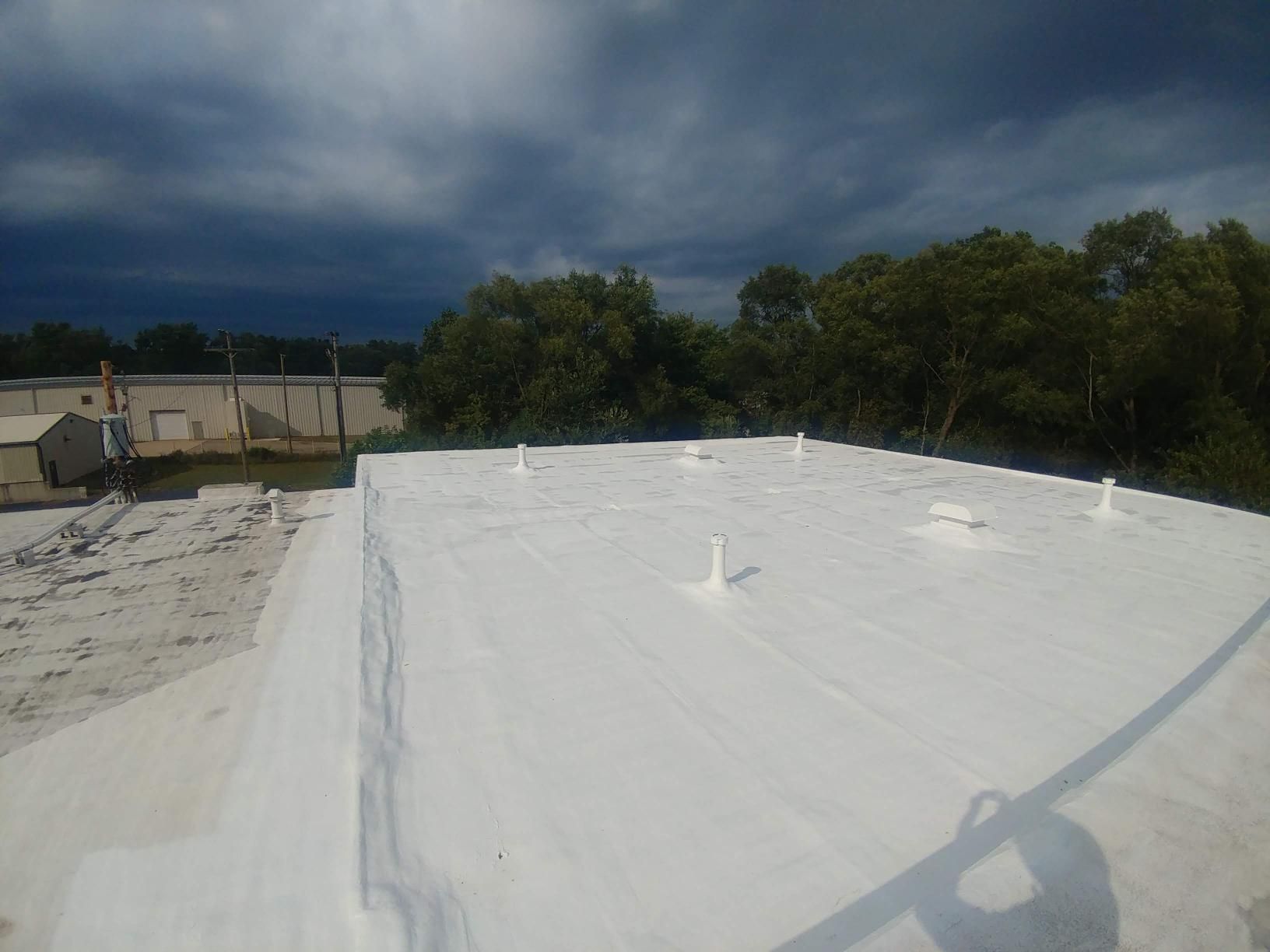 A white roof with trees in the background and a cloudy sky.