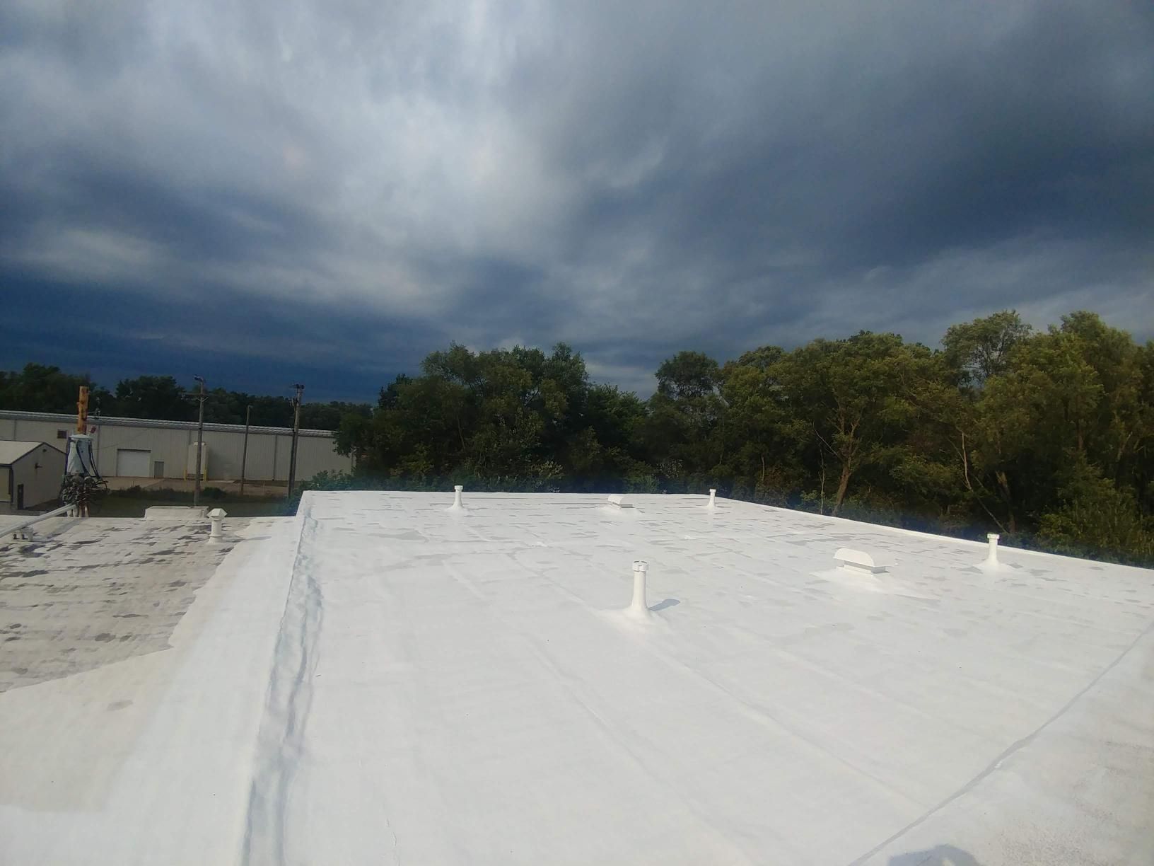 A white roof with trees in the background and a cloudy sky.