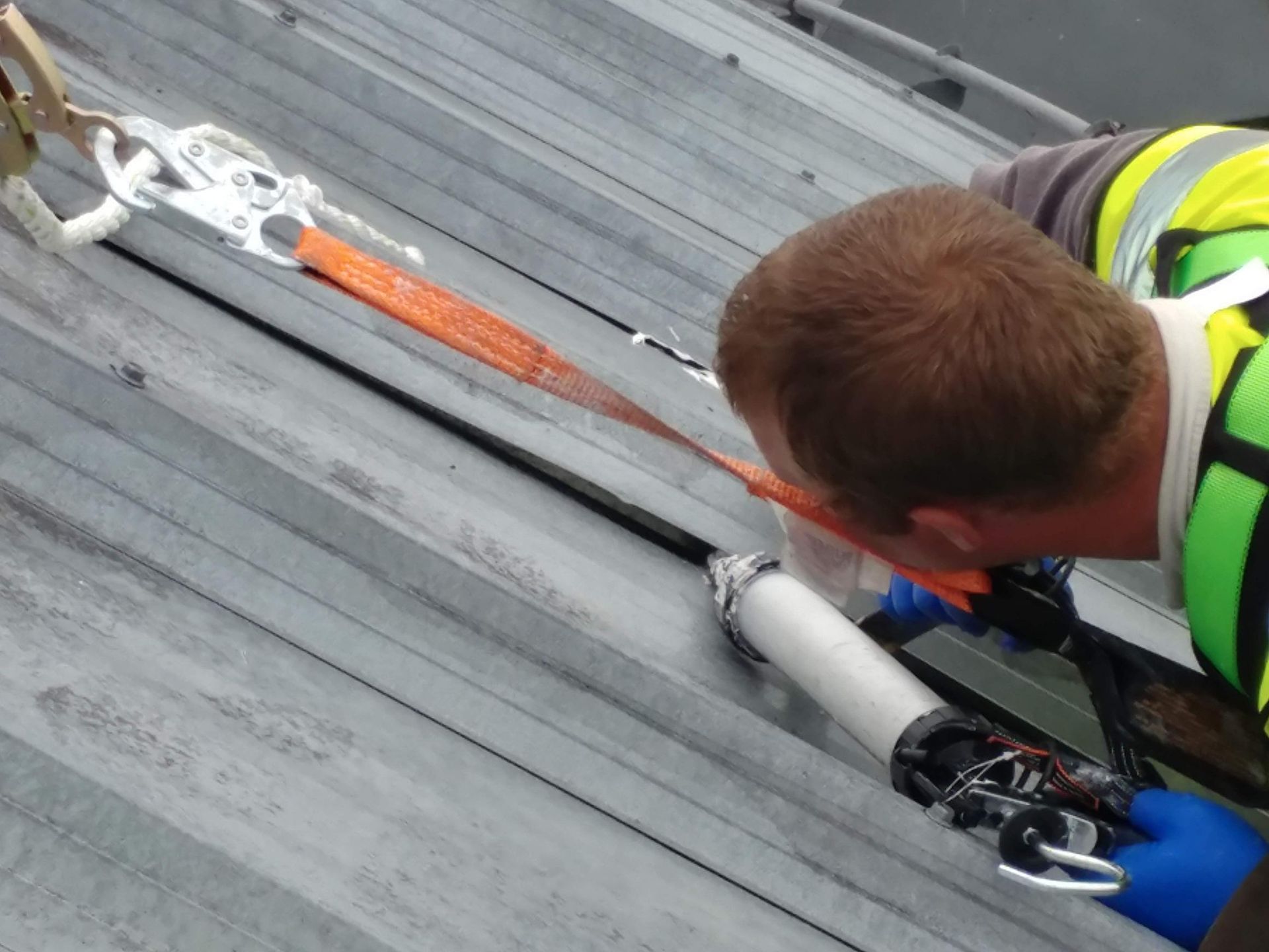 A man in a yellow vest is working on a roof