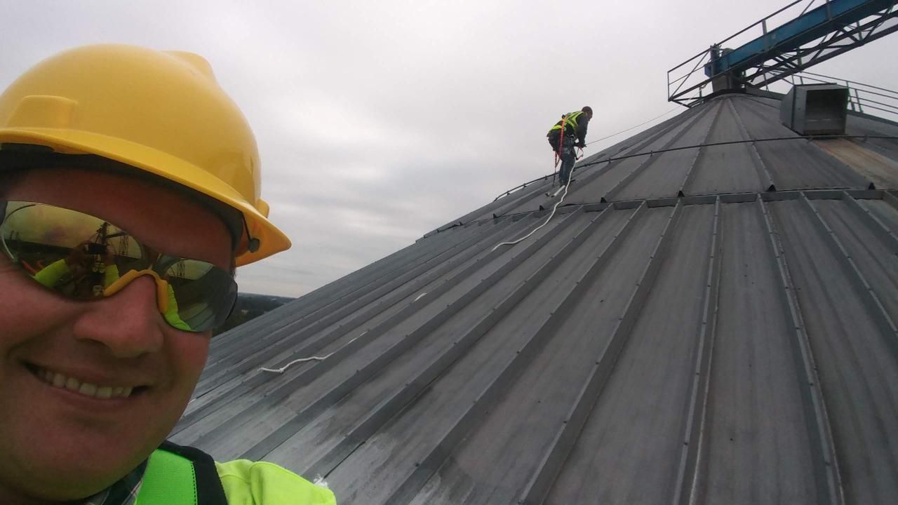 A man wearing a hard hat and sunglasses is standing on a roof.