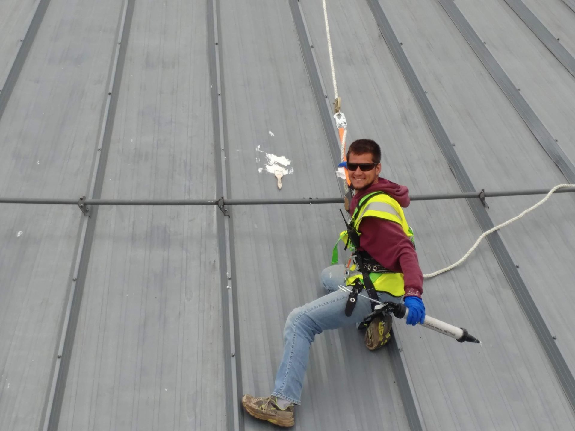 A man is sitting on a roof holding a tool