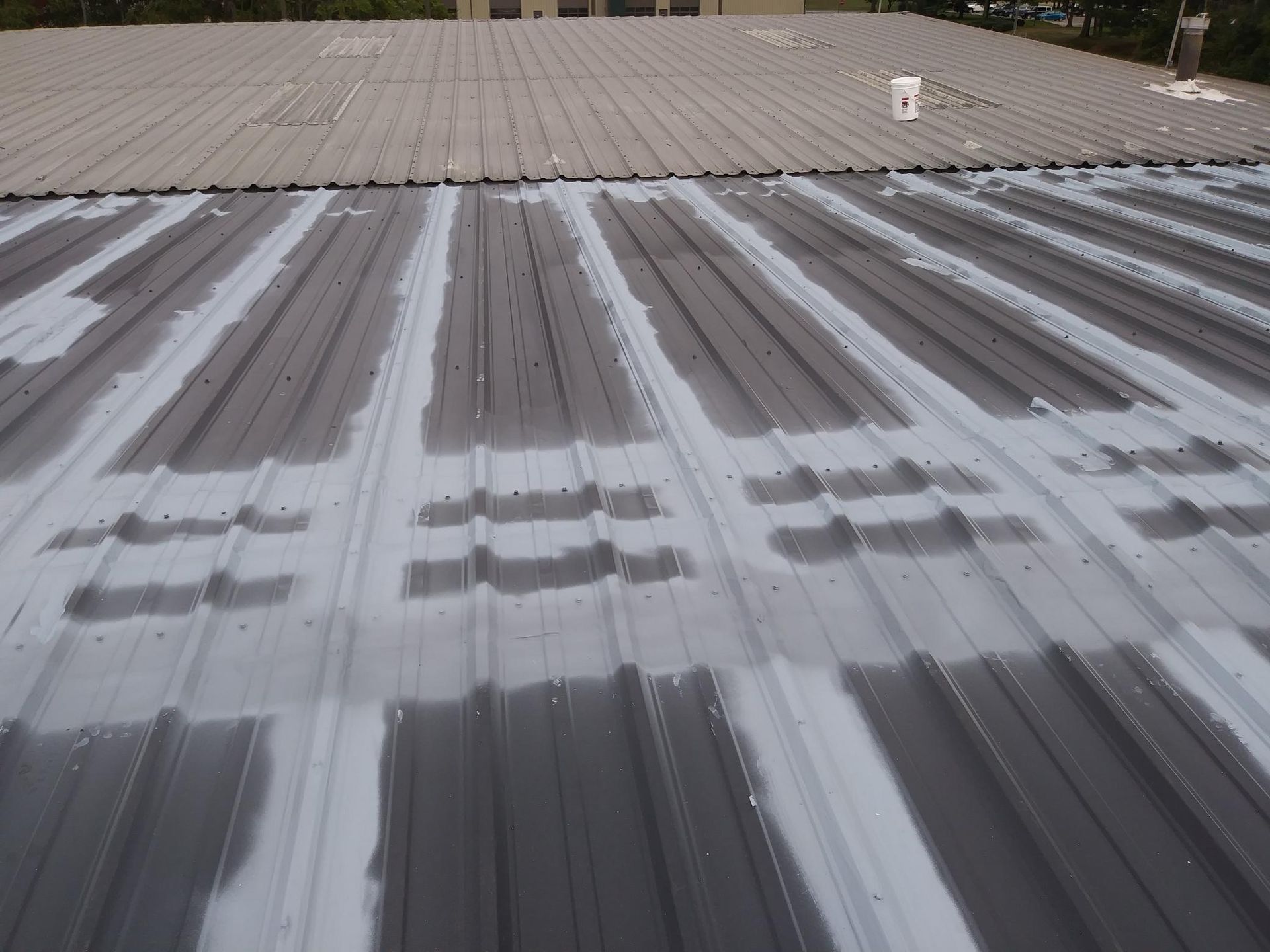 A metal roof is being painted with white paint.