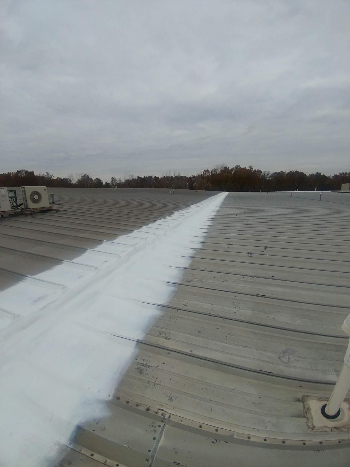 A roof is being painted with white paint on a cloudy day.