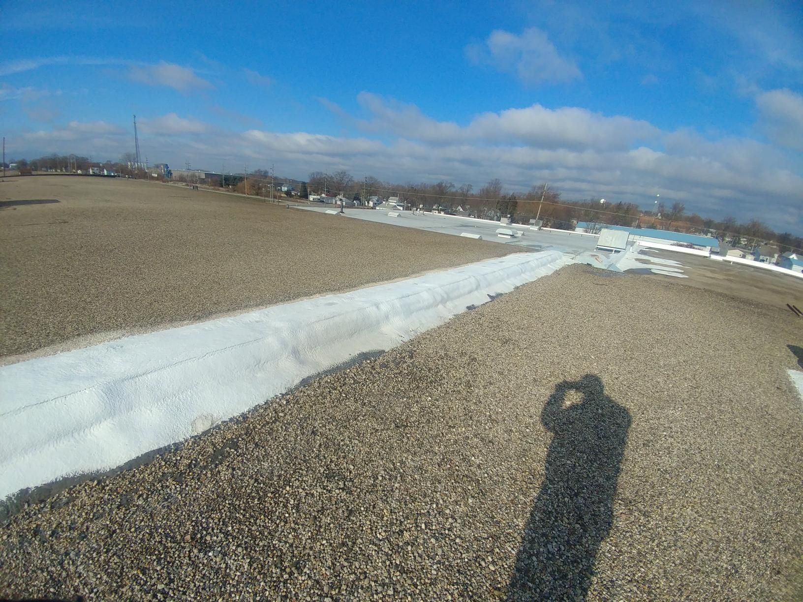 A person is taking a picture of their shadow on a gravel road.