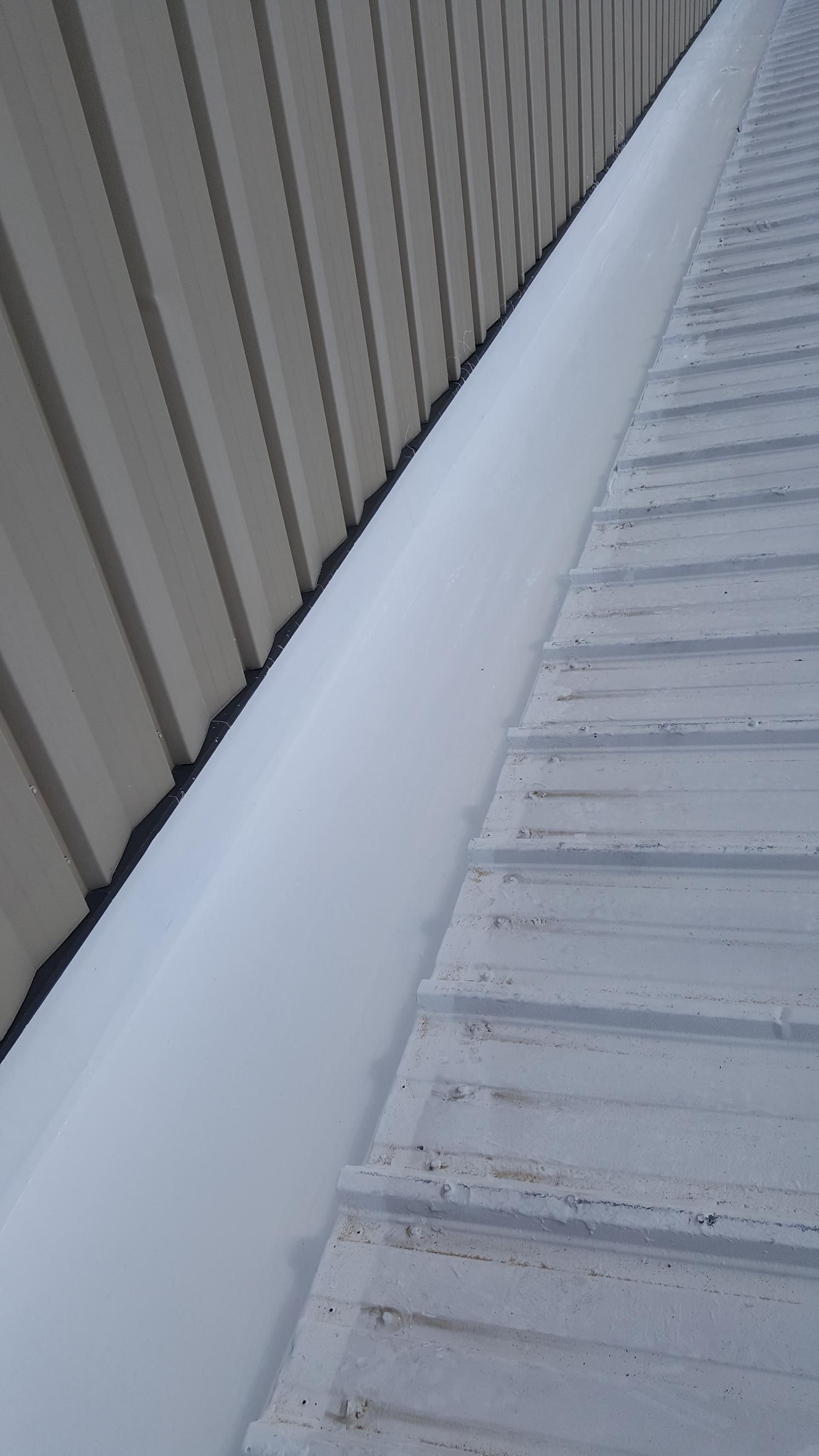 A white gutter on the side of a building next to a white roof.