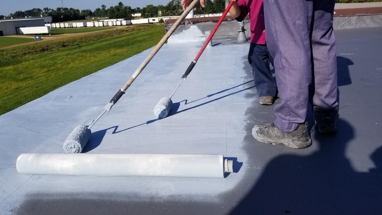 Two people are painting a roof with rollers.