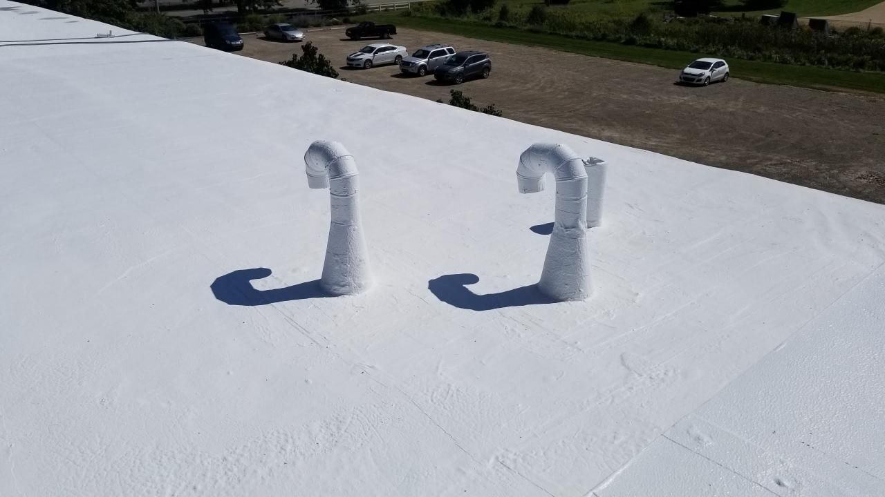 A white roof with two pipes on it and a parking lot in the background.