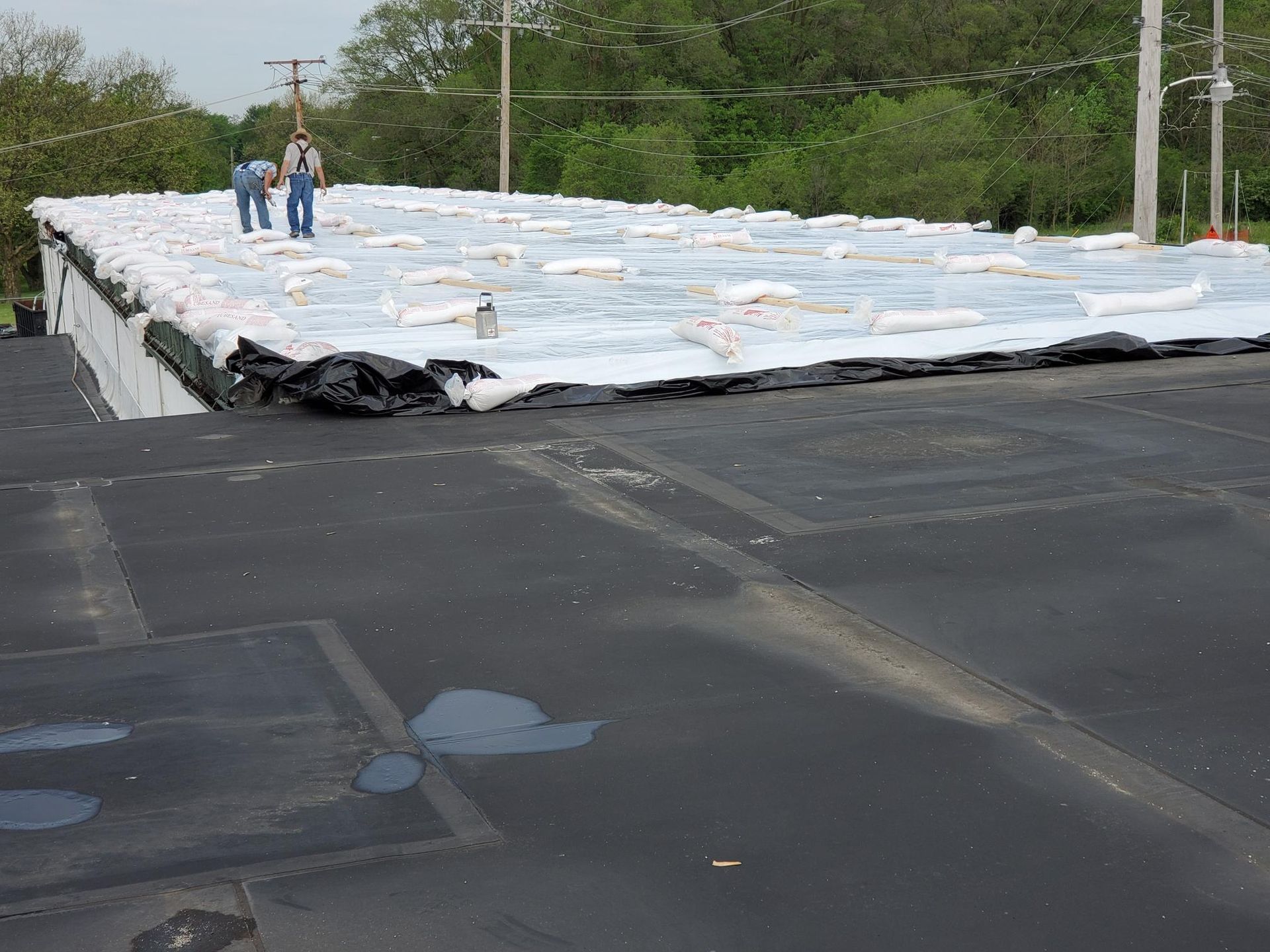 Two men are standing on top of a roof covered in plastic bags.
