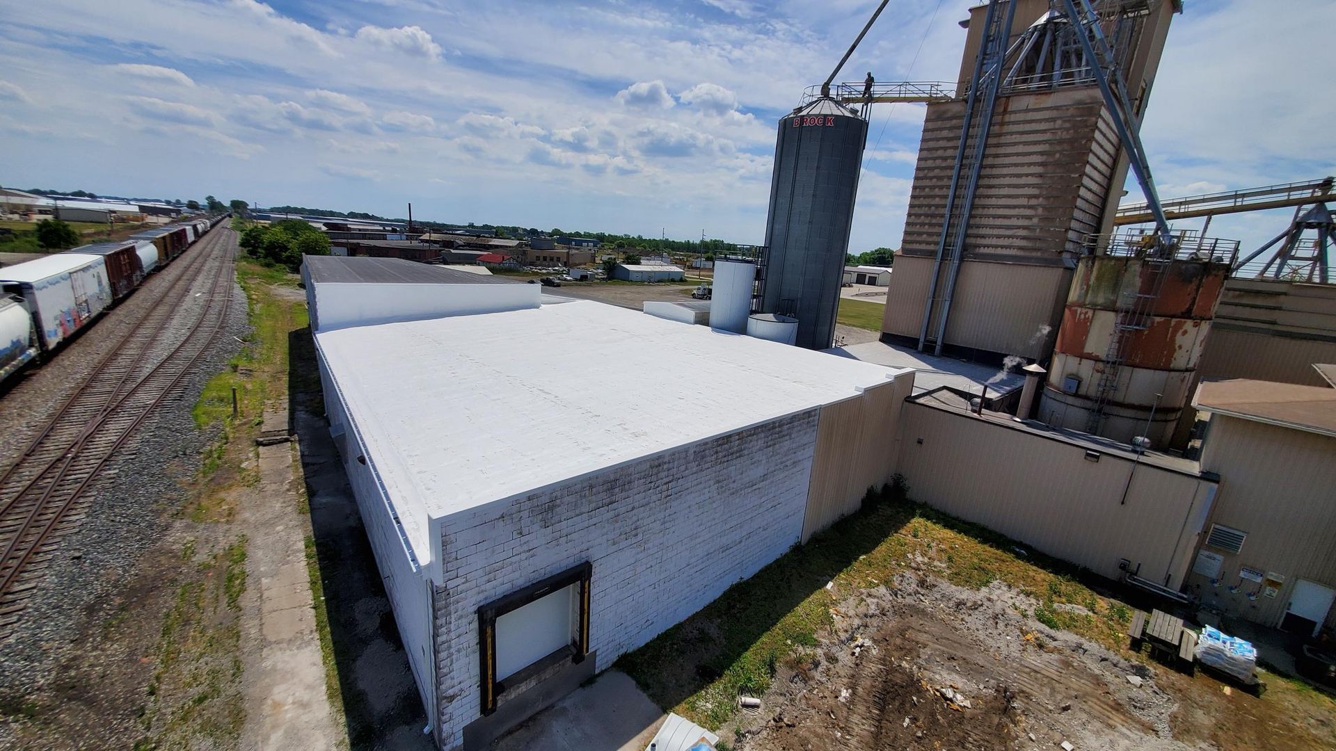 An aerial view of a building with a white roof next to train tracks.