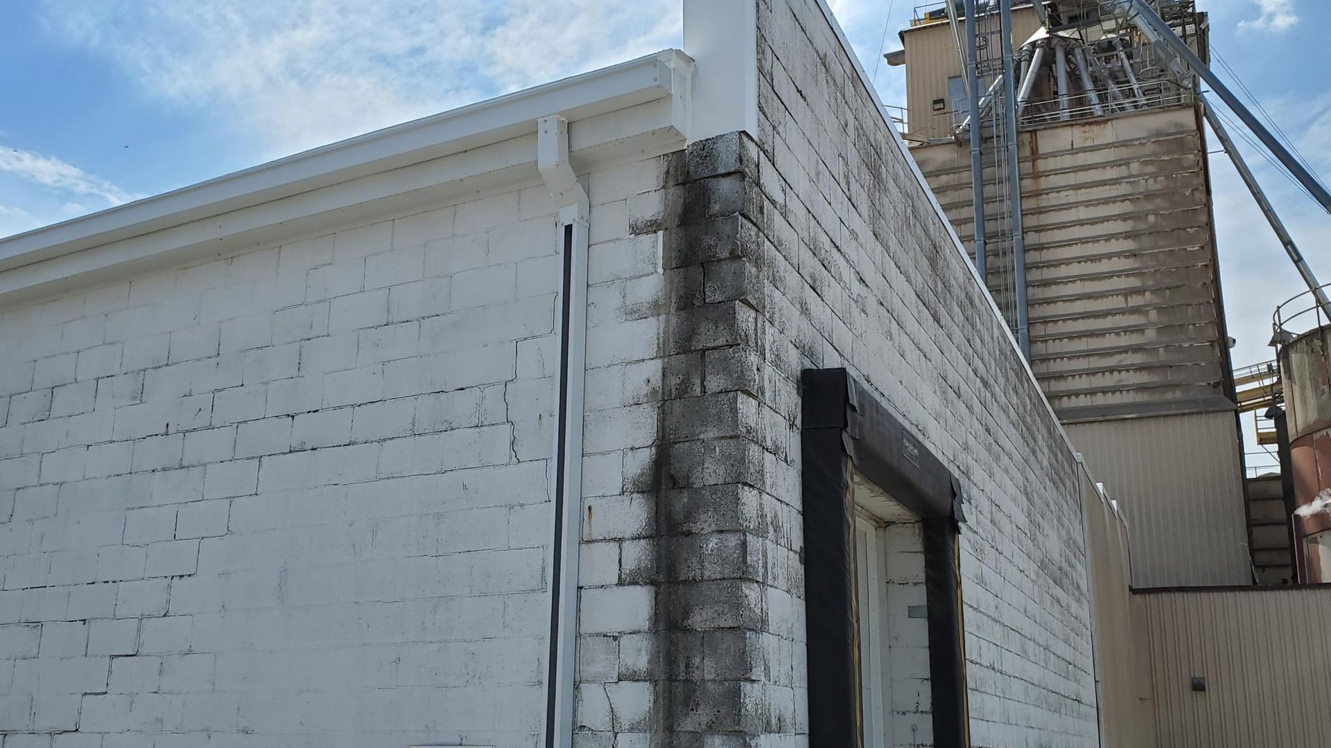 A white brick building with a window and a silo in the background