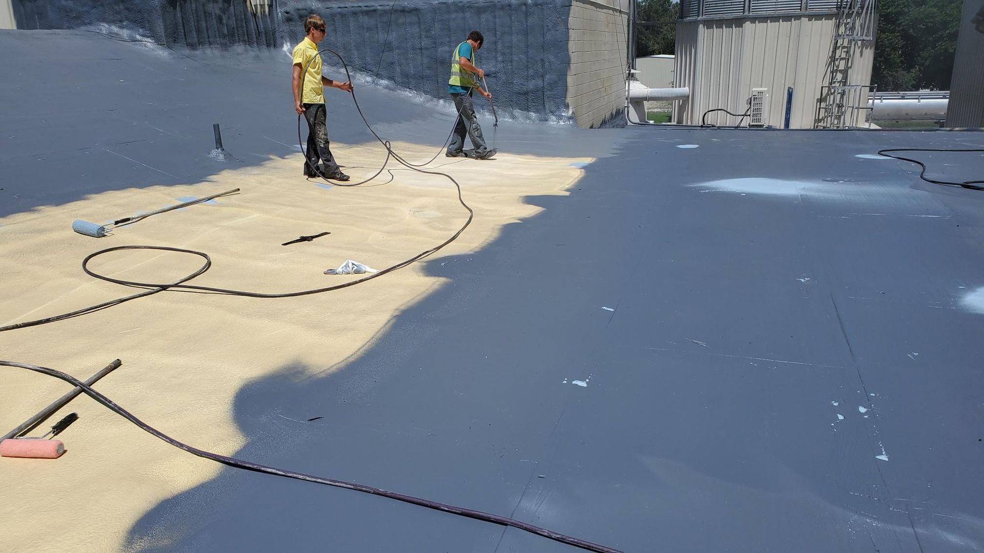 Two men are painting a roof with a sprayer.