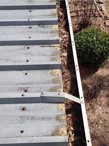 A metal roof with a white gutter and a bush in the background