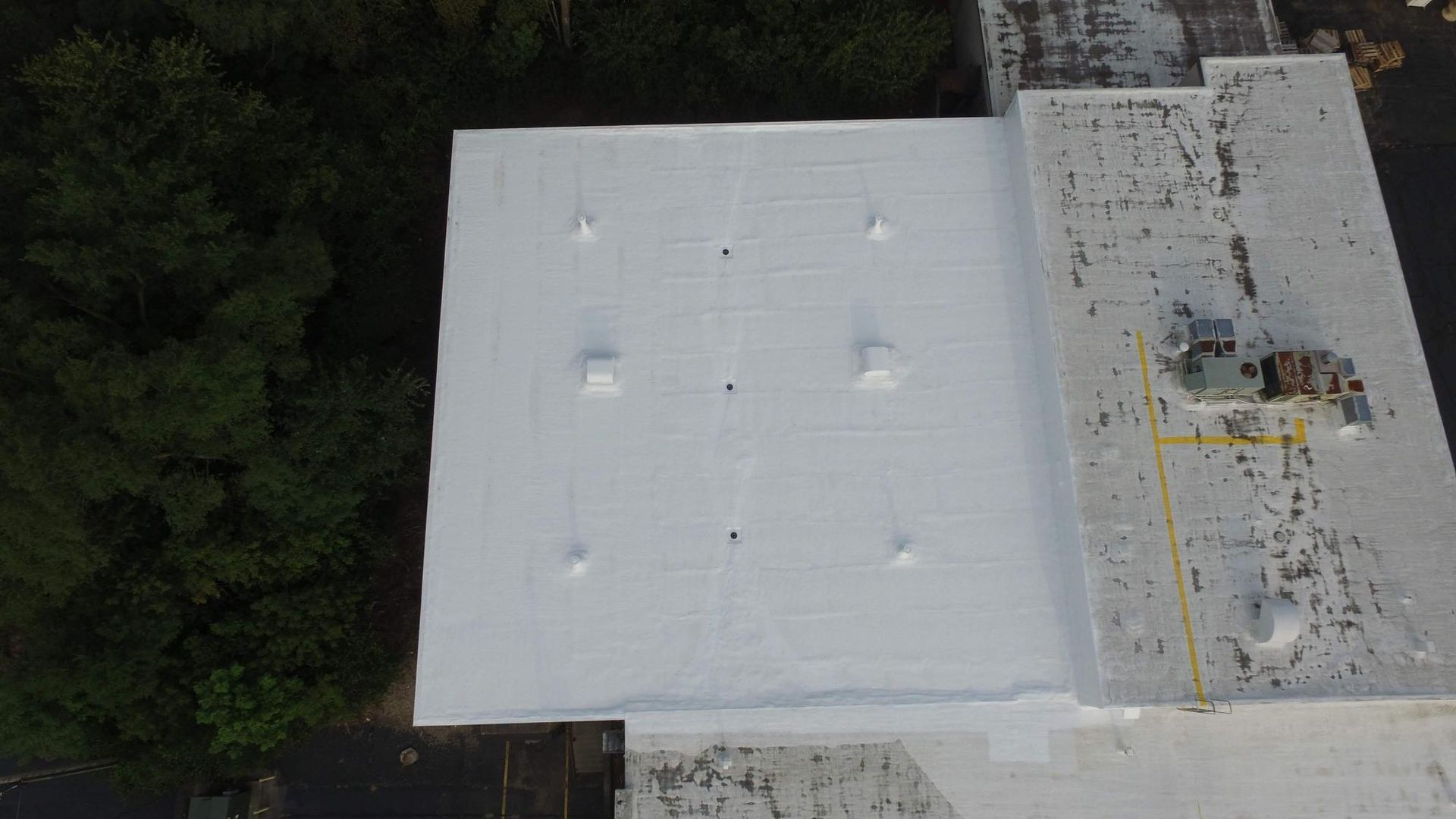 An aerial view of a large white roof with trees in the background.